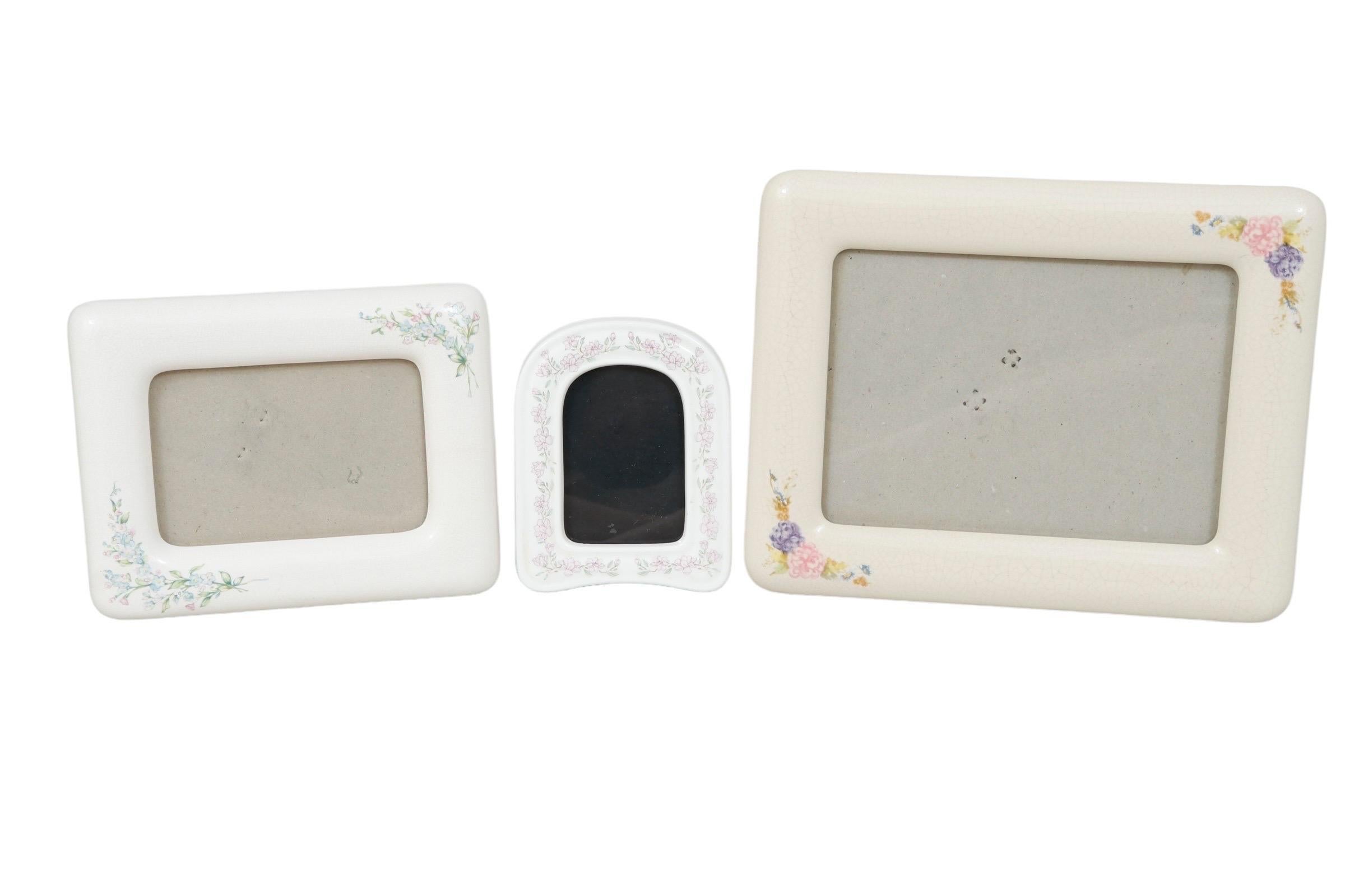 A set of three coordinating ceramic photo frames. Varying shades of off-white are decorated with floral sprays. Frames measure between 3.75