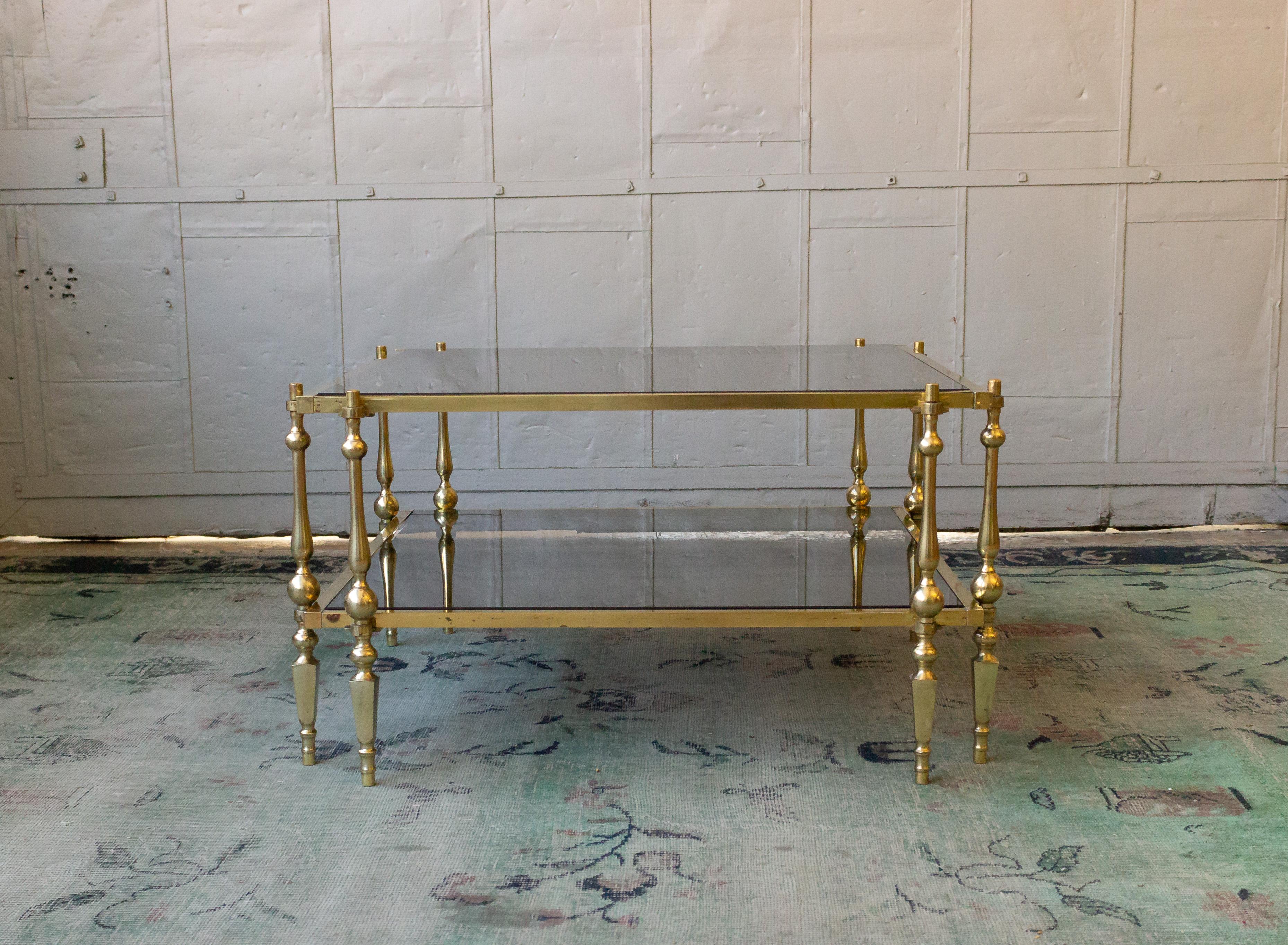 This 1980s French brass and glass coffee table is a striking representation of vintage design. The square brass frame supports a smoked black glass shelf and top, creating a bold contrast that adds depth and intrigue to any space. Hailing from