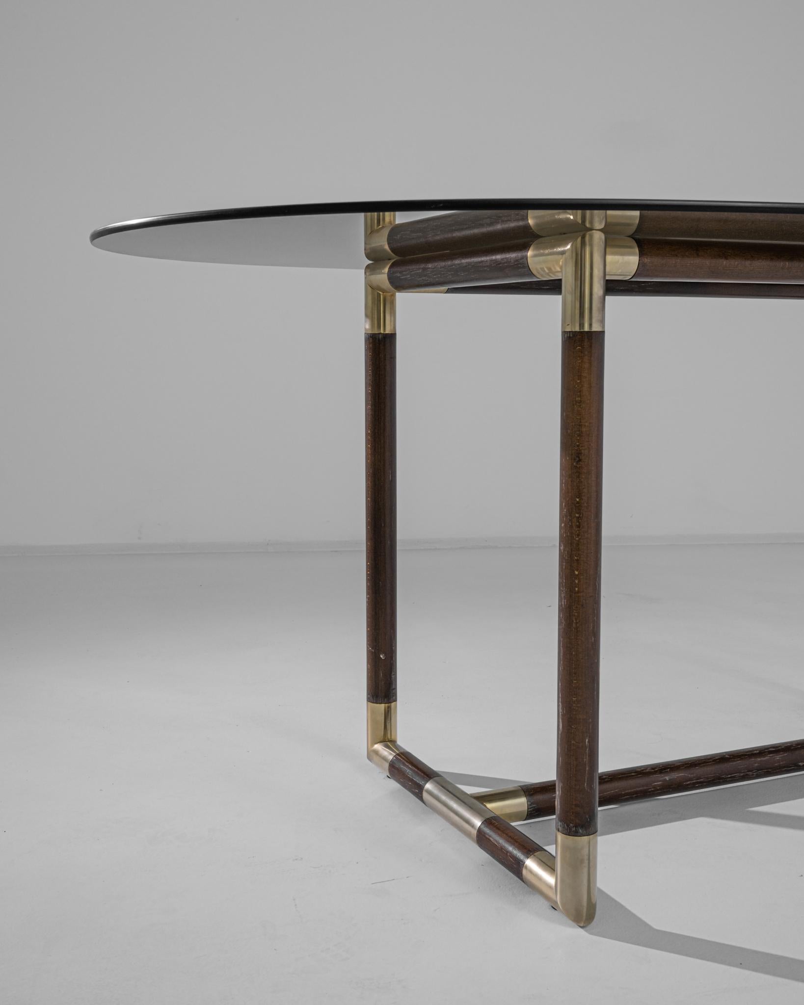 A coffee table made in France circa 1980. The tubular wooden base decorated with gilded tips constitutes a three-dimensional rectangular silhouette, juxtaposing against the oval shape of the smoked glass table top. Exuding an Art Deco aesthetic,