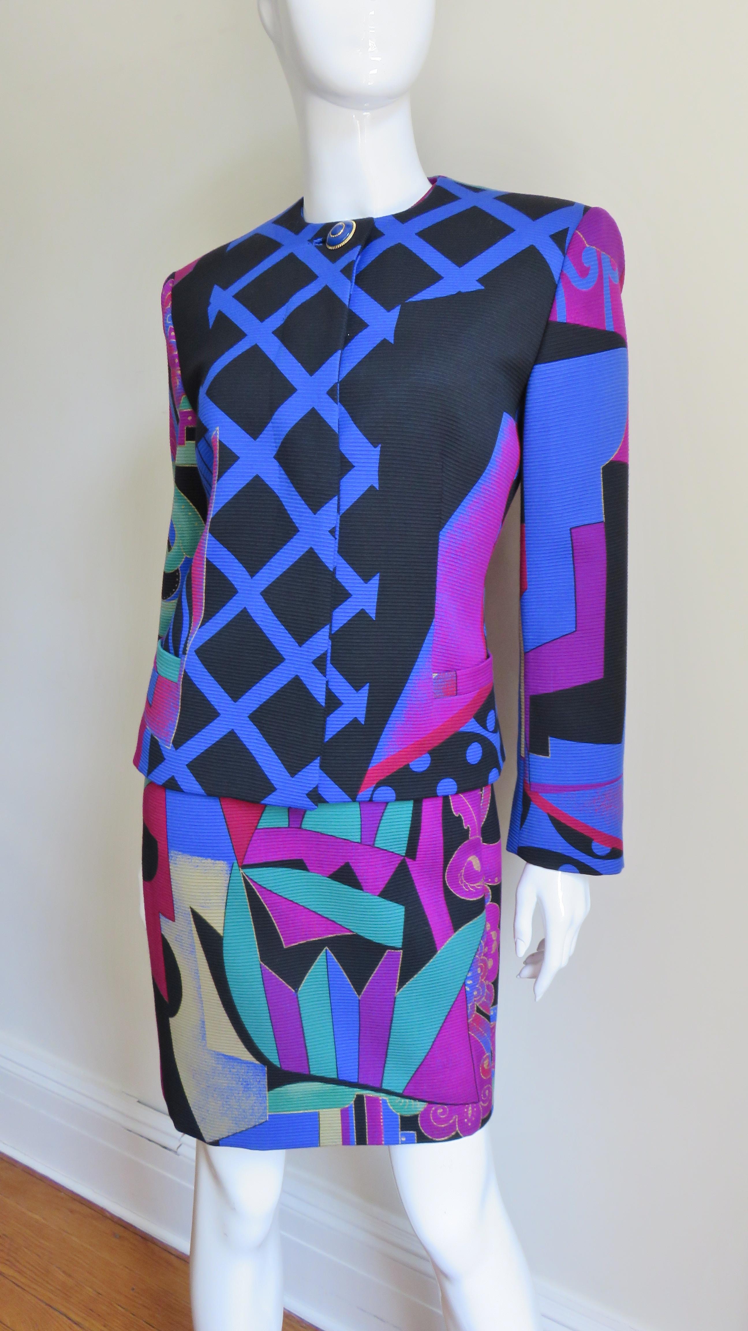 A brightly colored abstract pattern light weight wool dress and jacket set from Gianni Versace in blue, red, purple, green, yellow and black. The dress is semi fitted with a crew neckline and cap sleeves.  The collarless jacket has shoulder padding