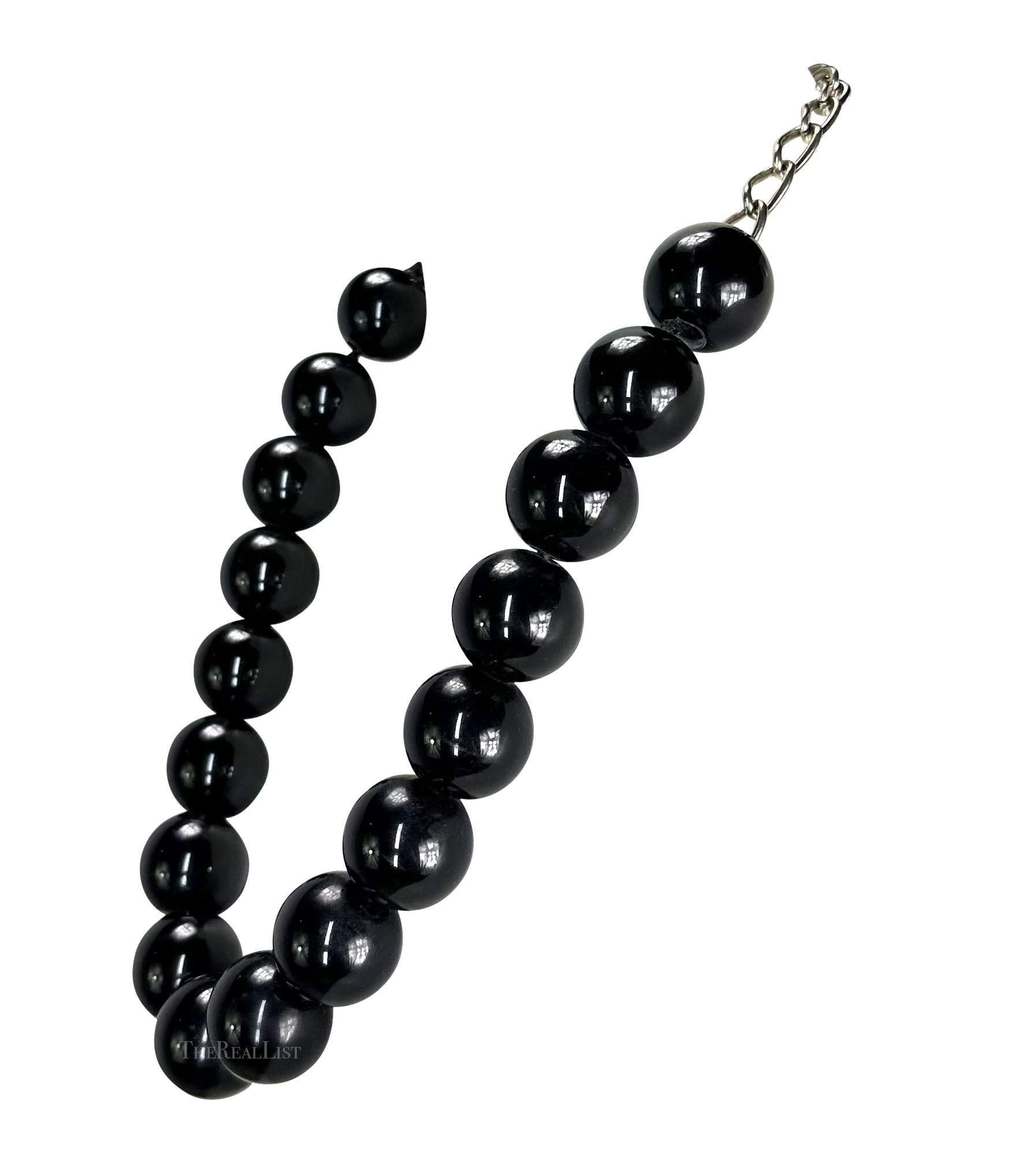 Ti presentiamo una bellissima collana di perline nere di Gianni Versace, disegnata da Gianni Versace. Questa collana, risalente alla fine degli anni '80, presenta un filo di grandi perle nere ed è completata da una chiusura a catena color argento.
