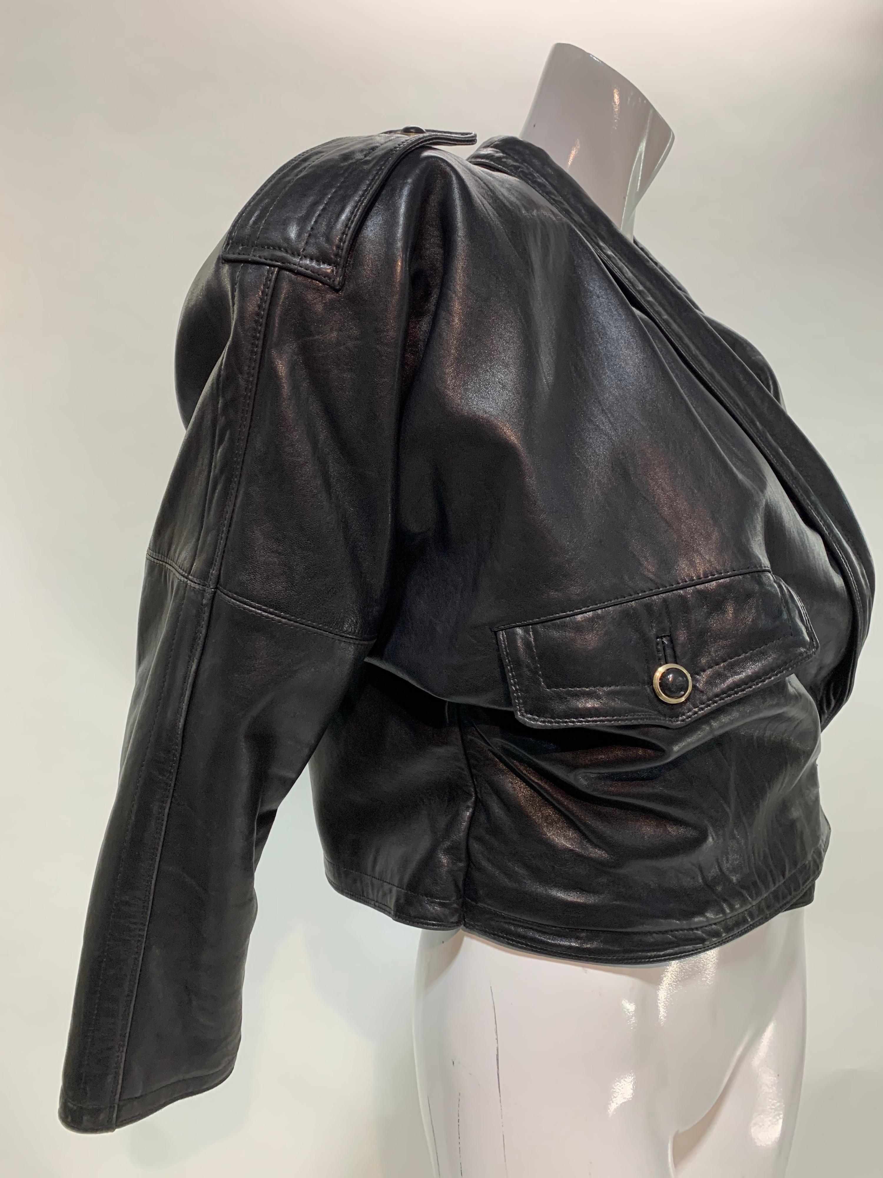 Chaqueta Gianni Versace oversize de estilo motero de piel negra de los años 80 con solapas espectaculares, silueta de hombros acolchada y estructurada, capucha trasera y forro de fieltro de cachemira. Cinturón con hebilla lateral asimétrica. Mangas