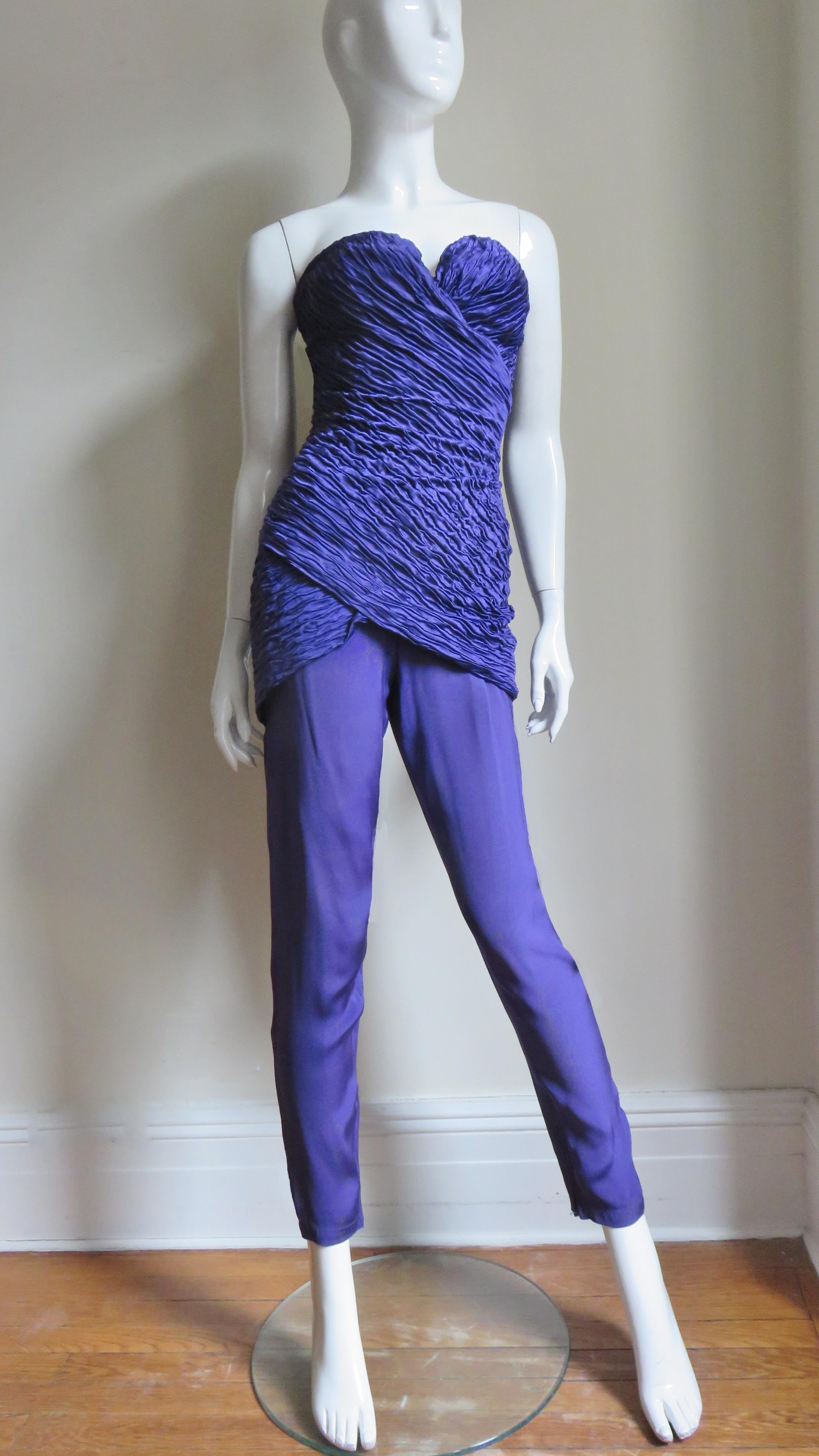 A fabulous purple silk strapless bustier jumpsuit from an early Gianni Versace collection. The fitted, micro pleated, boned bustier bodice crosses and wraps at the bust. The slim pants portion have ankle zippers.  It is fully lined in same fabric,