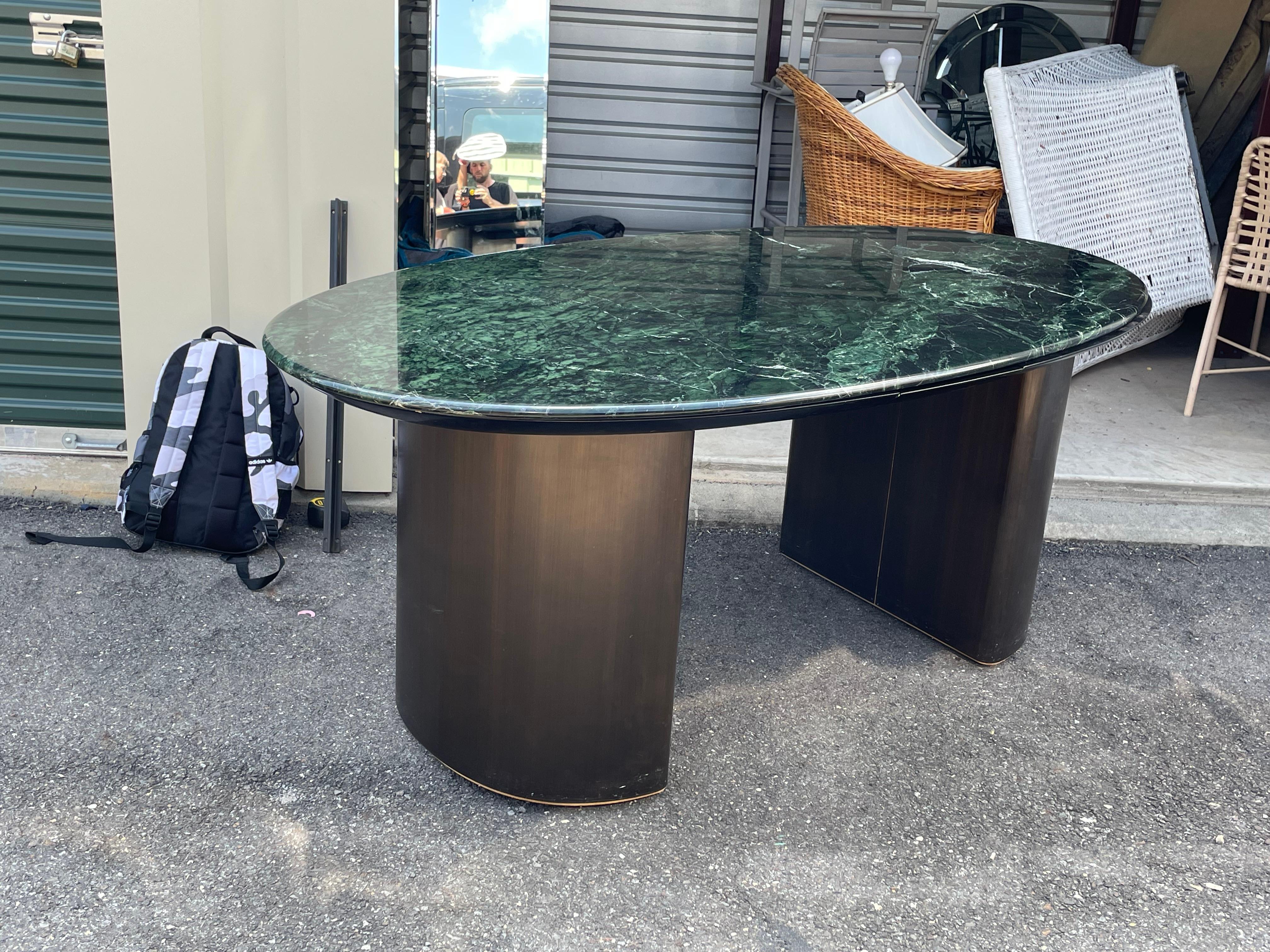 Exquisite desk in the manner of Gilbert Rohde features an amazing green Italian oval marble top which sits on 2 bronze half moon pedestals also has a small storage drawer 