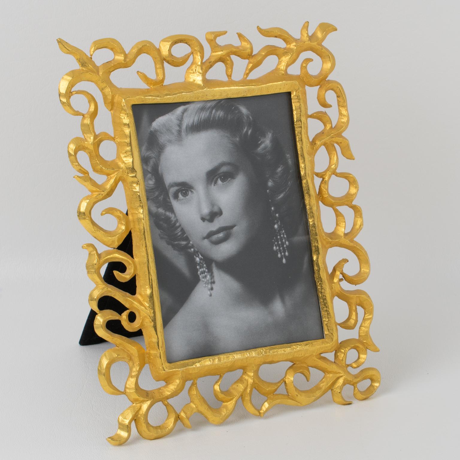 Elegant gilt metal picture photo frame by French designer Edouard Rambaud. Dimensional shape in brushed gilt metal with carving and see-thru detailing. Back and easel in black velvet. Signed underside with 
