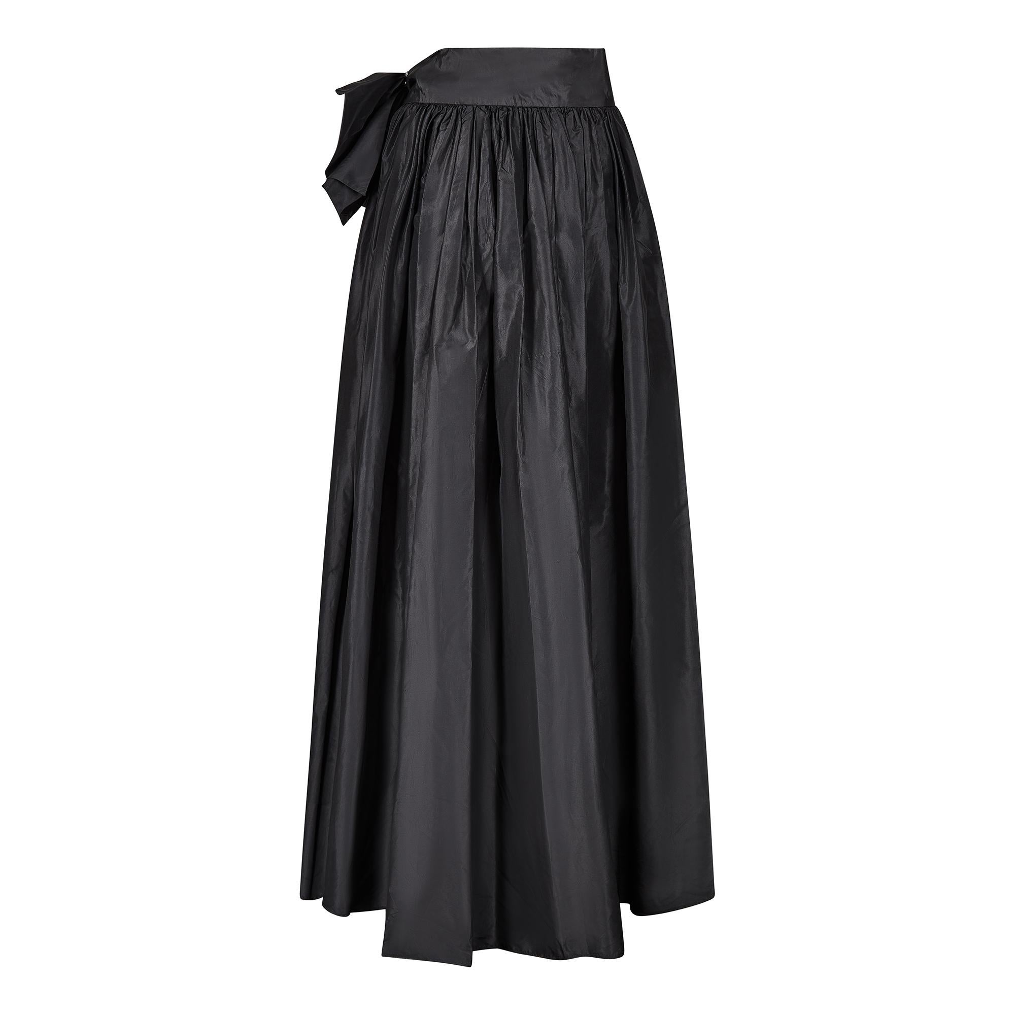 This 1980s black silk taffeta Gina Fratini skirt is a dramatic interpretation with very striking design elements including an asymmetric hem that is shorter at the front with a gentle curving train at the back. It has a gathered waistline that is