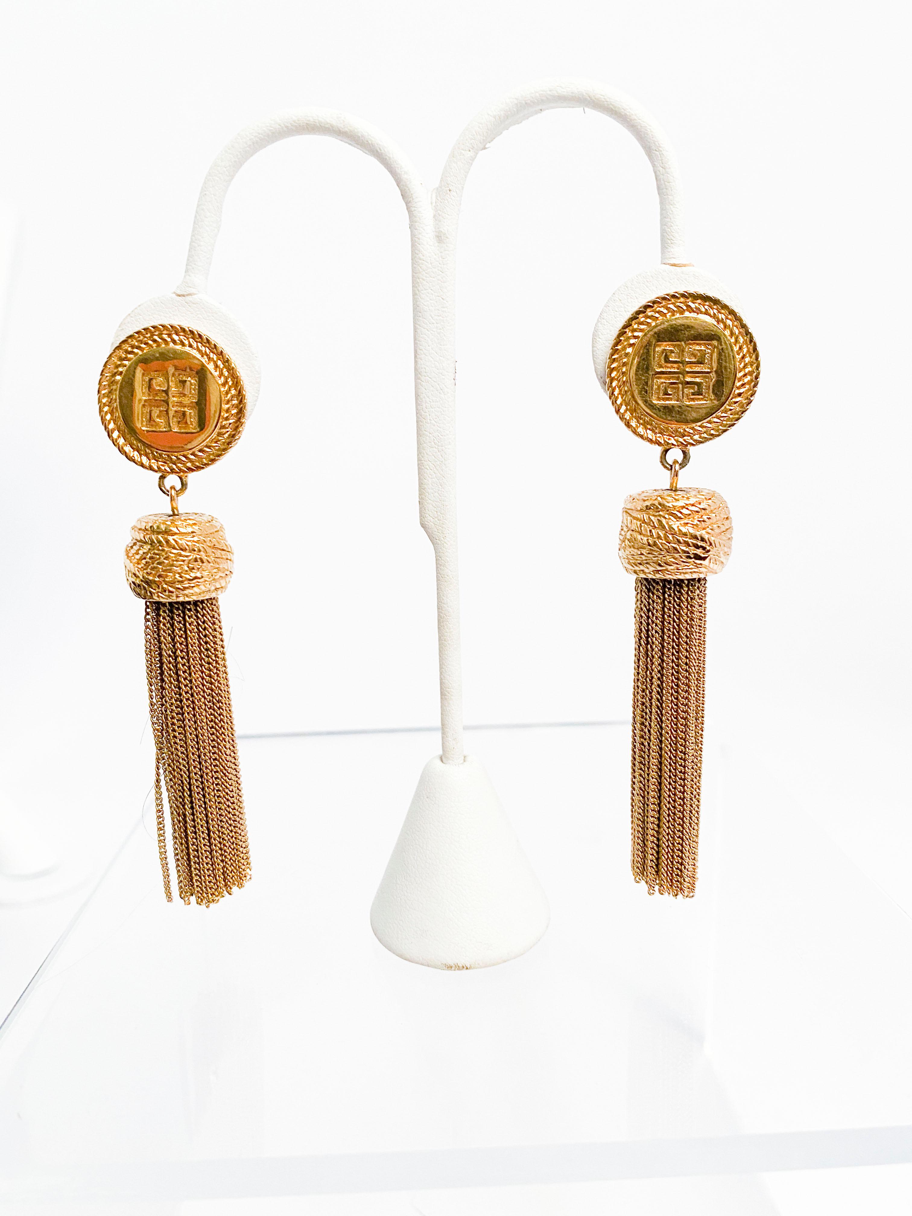 1980s Givenchy gold-tone clip on earrings with long chain tassels. The main ear piece is circular in shape with the Givenchy house emblem centered.