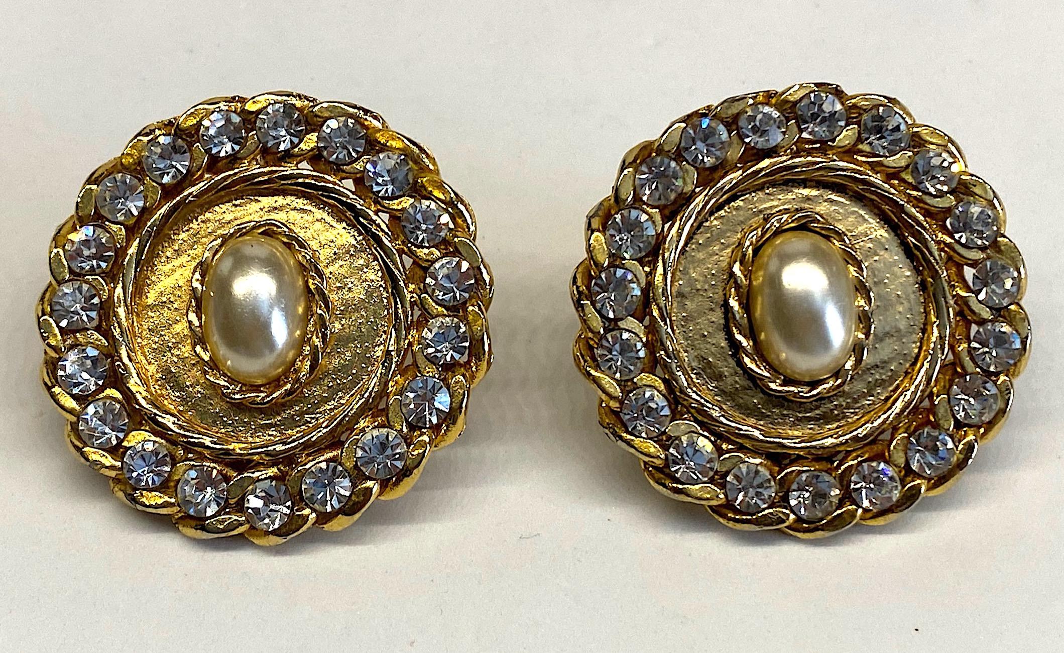 A large pair of 1980s button medallion earrings. Each earring is 1.75 inches in diameter and has an oval faux pearl cabochon in the center. The pearl is surrounded by a rope twist braid and matching curb link chain set with rhinestones. They are
