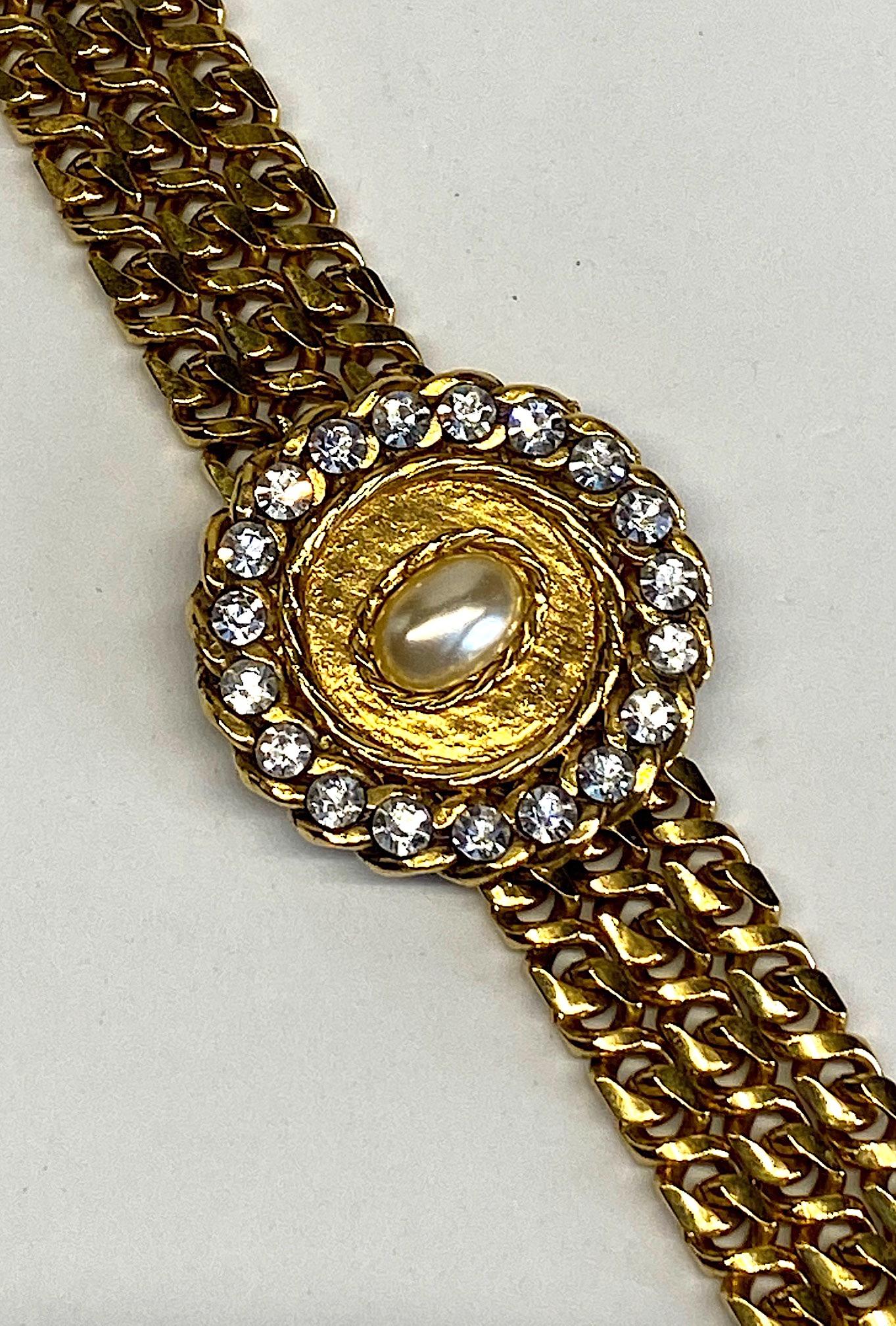 Bracciale a catena a tre fili degli anni '80 con grande medaglione centrale. Ognuno dei tre fili di catena dorata misura 0,25 pollici di larghezza e 0,13 pollici di spessore. Il grande medaglione centrale misura 1,63 di diametro. Ha una perla finta