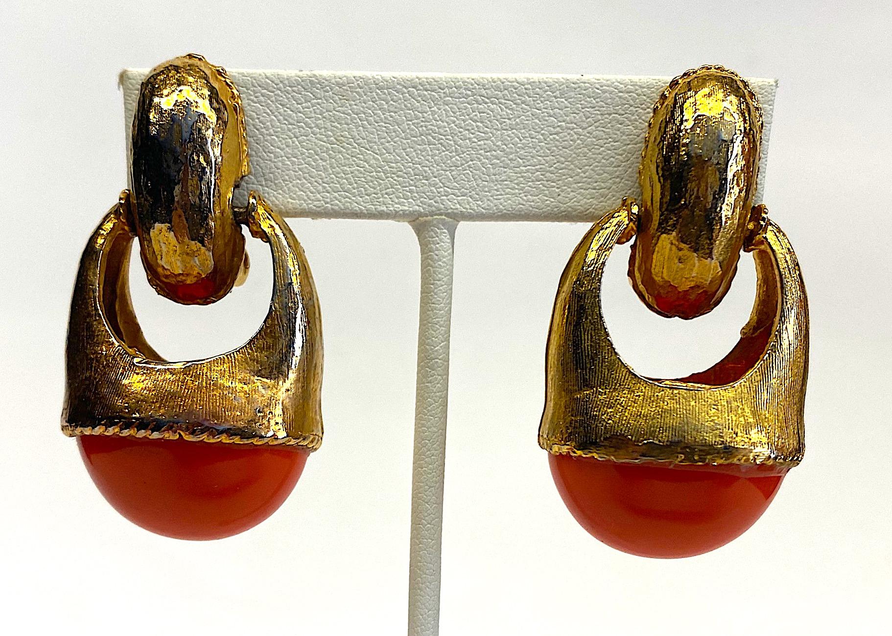 A stylish and chic pair of late 1980s door knocker style dangle earrings in gold plate with large faux coral cabochon. The surface of the earring have tiny lines etched lines etched into them giving the gold tone a soft satin texture and look. The