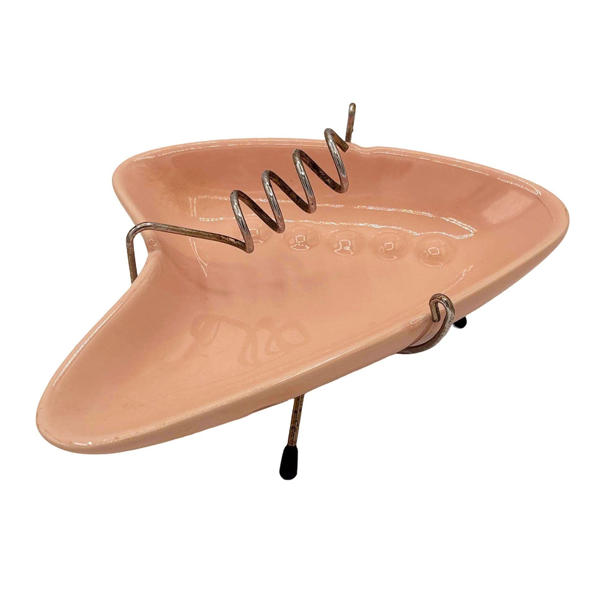 Googie Style Boomerang Shaped Ashtray Chrome Tripod Stand by OGGI featuring a pink boomerang-shaped ashtray with a chrome tripod stand that doubles as a cigarette holder.

Signed: 