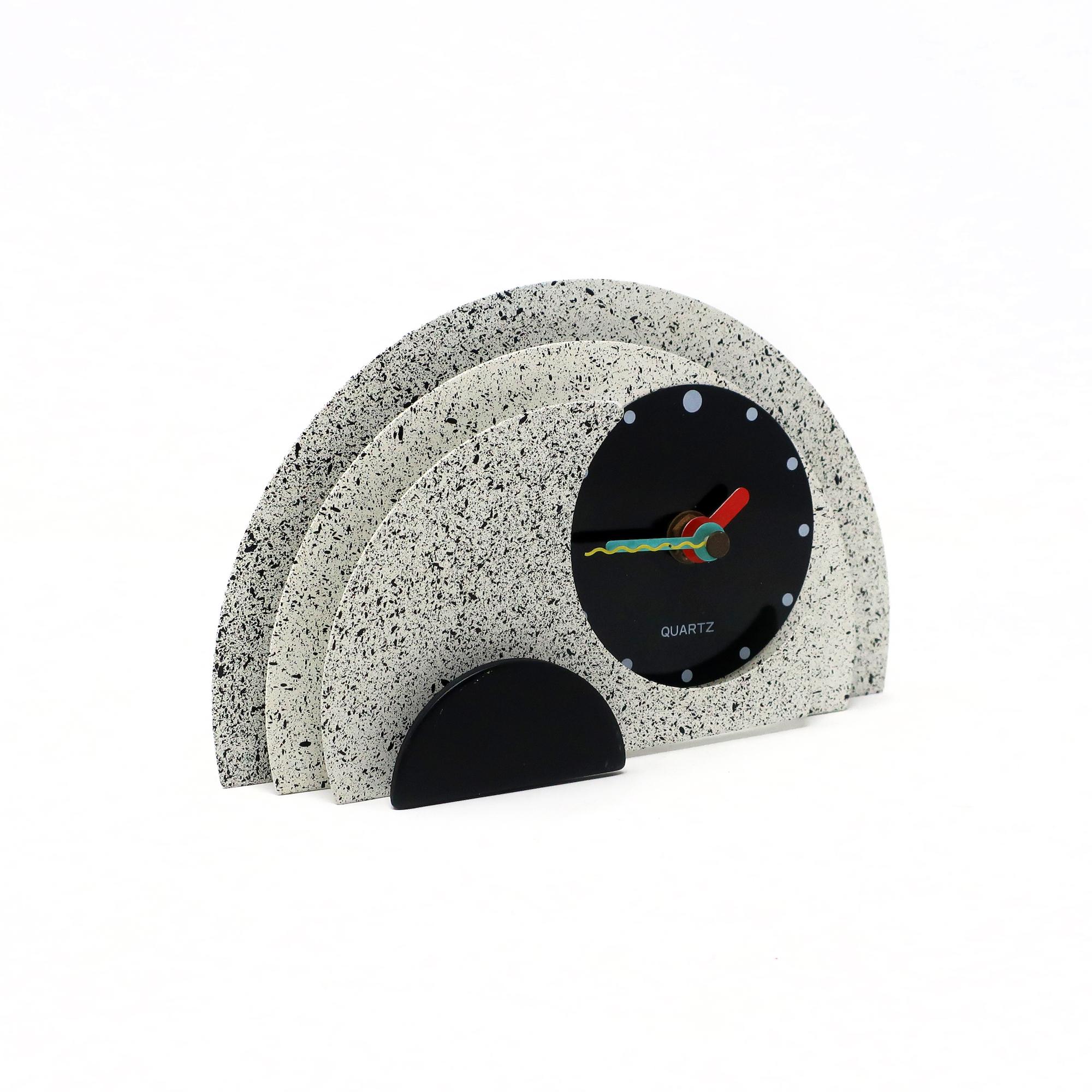 With a stunning combination of spotted gray and black enameled metal, black lucite accents, and primary colored hands, this postmodern clock is designed with a stacked semi-circle design that gives it a rare and beautiful three dimensionality. Bold