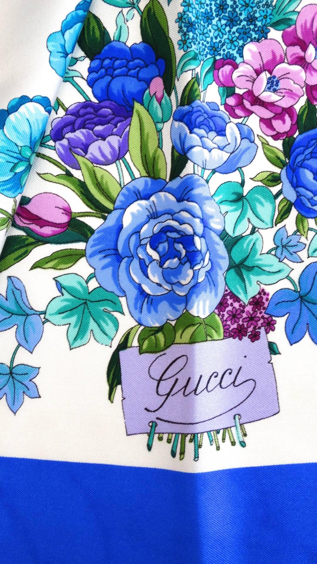 Rock a statement scarf with our incredible 1980s Gucci blue floral silk scarf! Solf silk fabric printed with a brilliant floral pattern in shades of teal, violet, and true blue. Trimmed with a thick blue border. Classic Gucci cursive signature