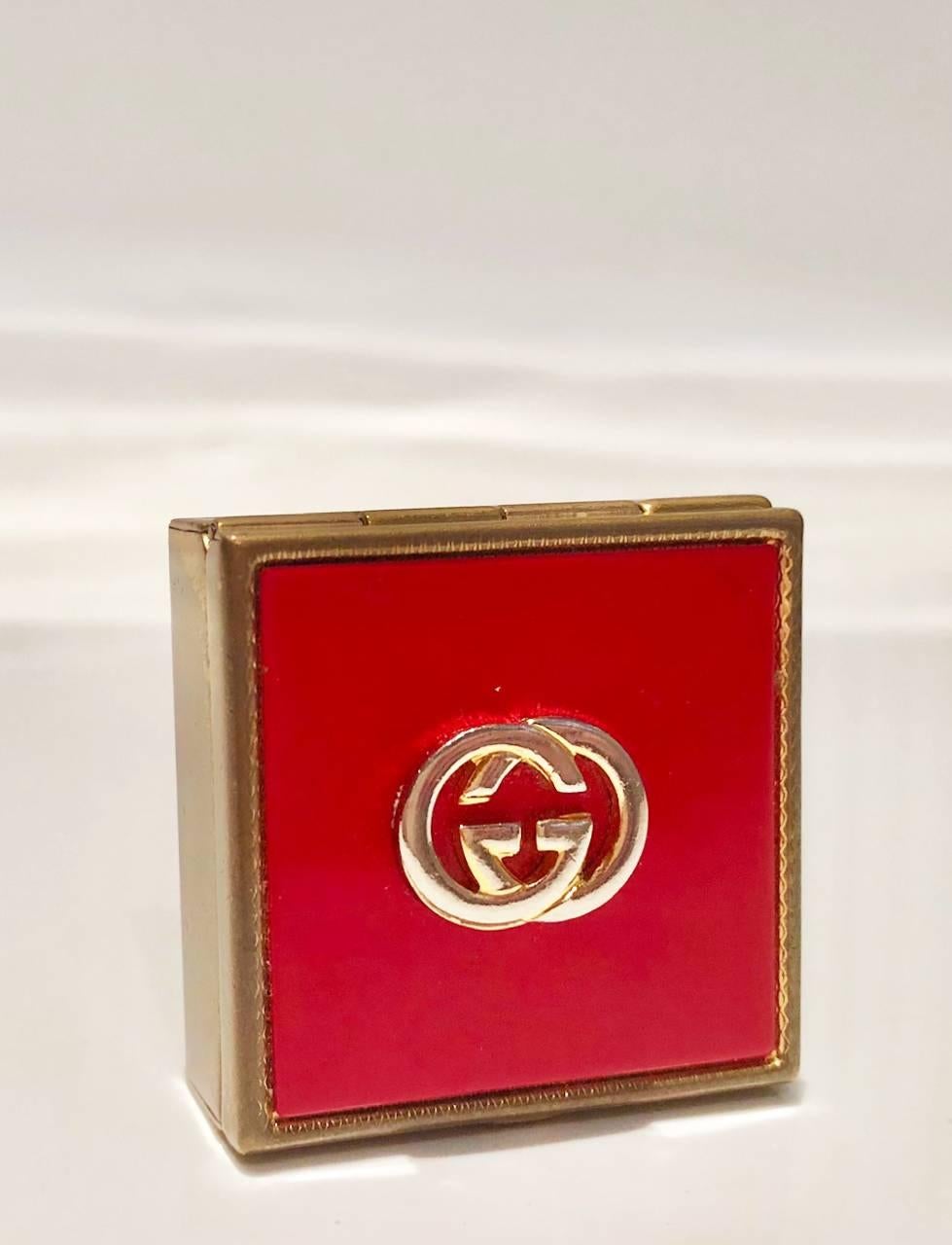 GUCCI GG metal interlocking logo square lidded Red and Gold tone metal pocket pill box / ashtray, enamel top, stamped Gucci signature on inner lid, cigarette holder swivel attached. A truly rare piece.

Dimensions: 3.8x3.8cm 
Condition: 1980s,