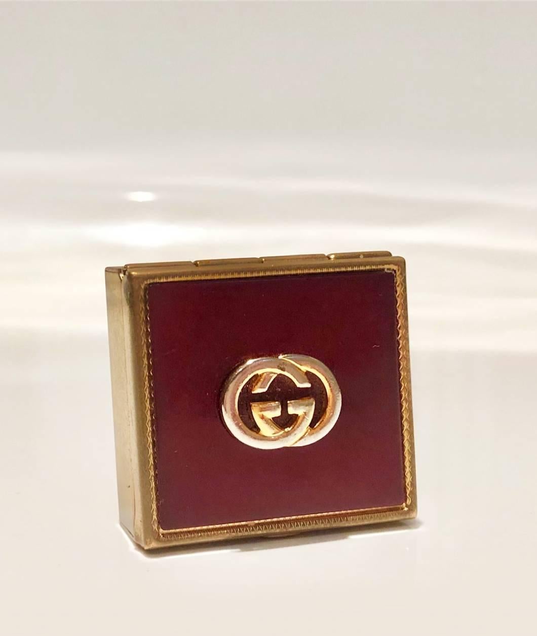 GUCCI GG metal interlocking logo square lidded Burgundy and Gold tone metal pocket pill box / ashtray / jewellery box, enamel top, stamped Gucci signature on inner lid, cigarette holder swivel attached. A truly rare piece.

Dimensions: 3.8x3.8cm
