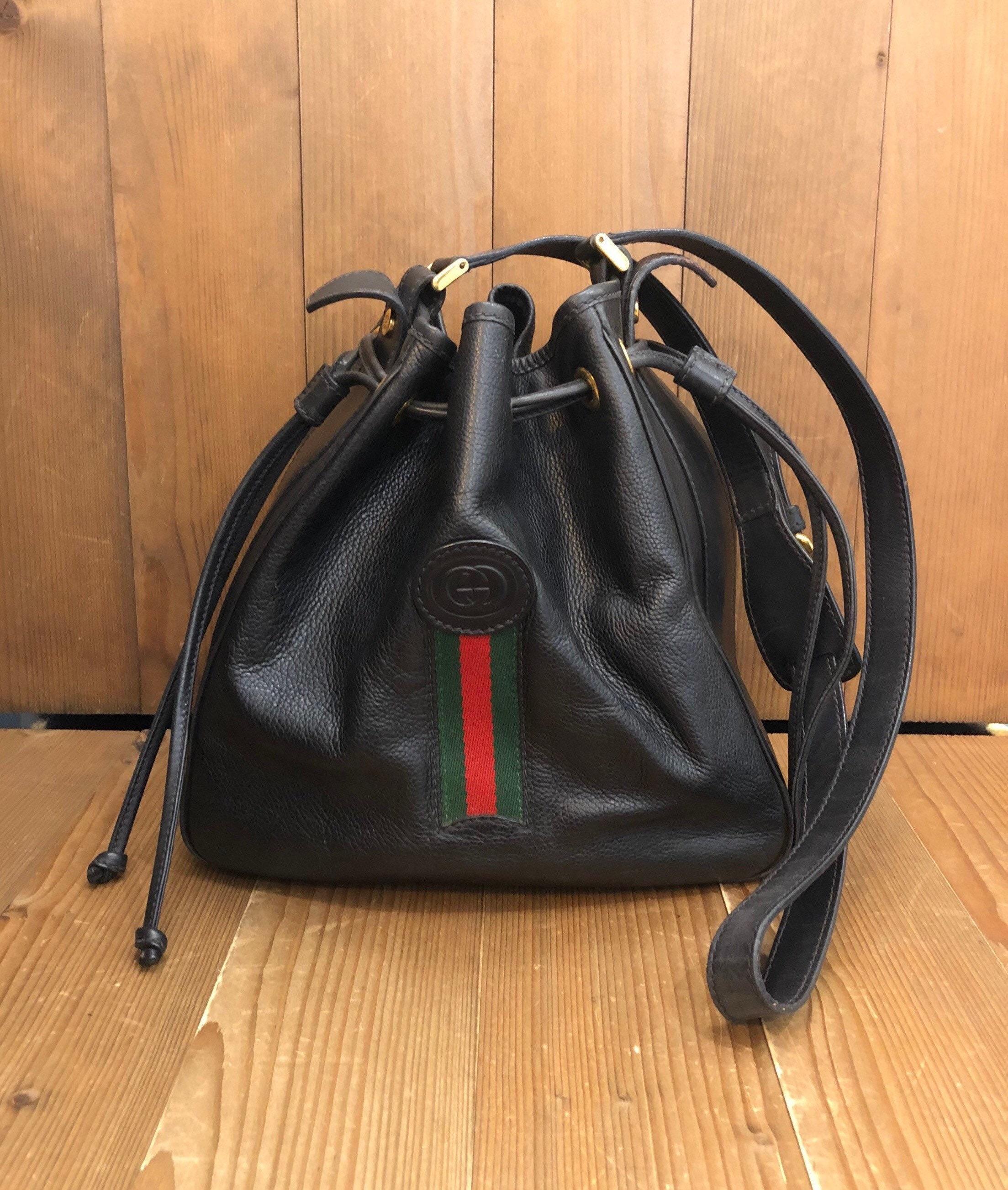 A vintage Gucci web bucket bag in black leather featuring an iconic Gucci Green/Red web on the front. Interior lined with luxurious suede featuring one interior zip pocket. Drawstring closure. Made in Italy. Measurement 10 x 9.5 x 5.75 inches Strap