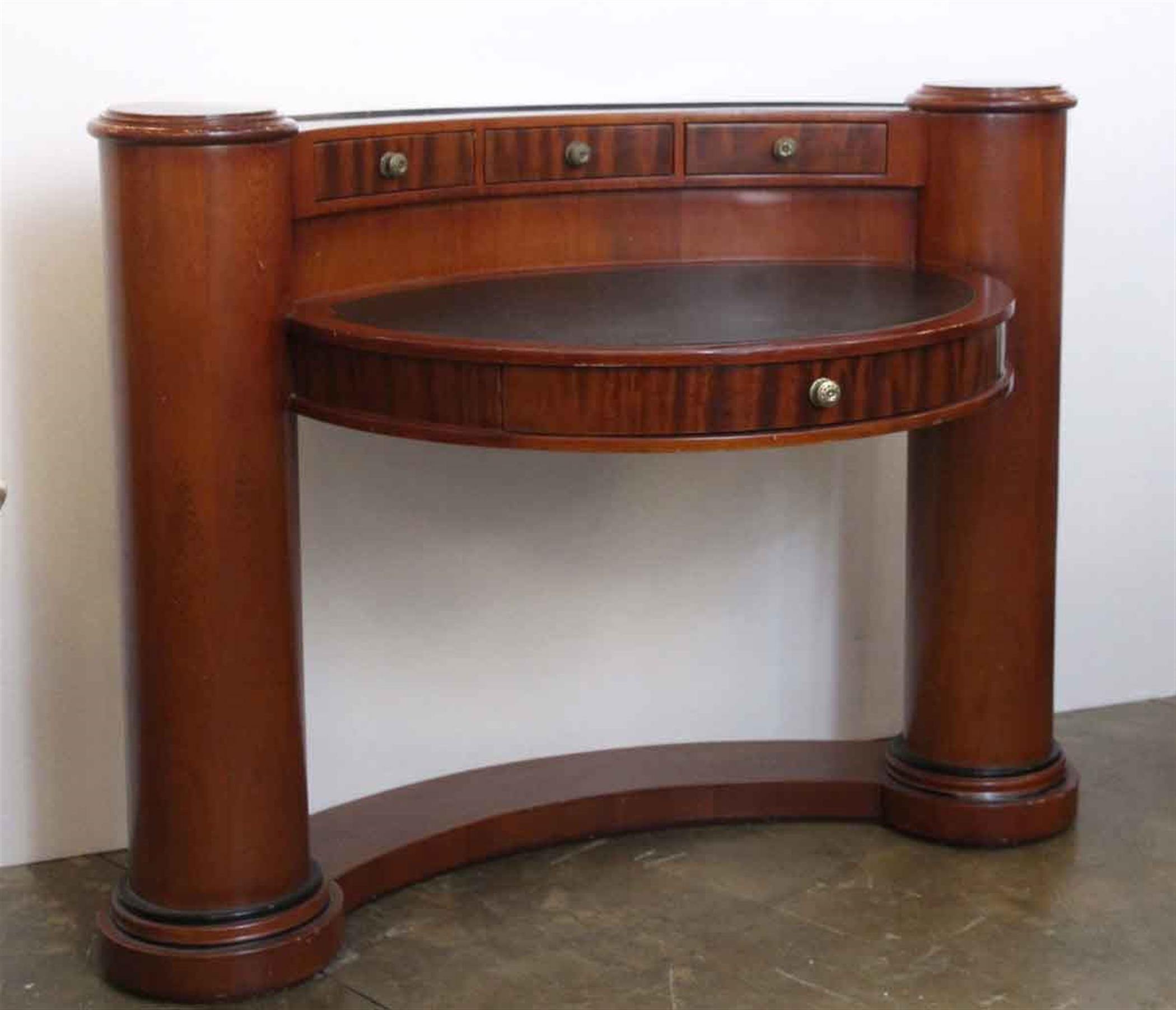 1980s dark wood tone half circle shaped desk with side pillars and black leather on the two top sections. It features three drawers at the top and one large center drawer. Handmade by Enrique Garcel in Colombia. There are minor chips and nicks in