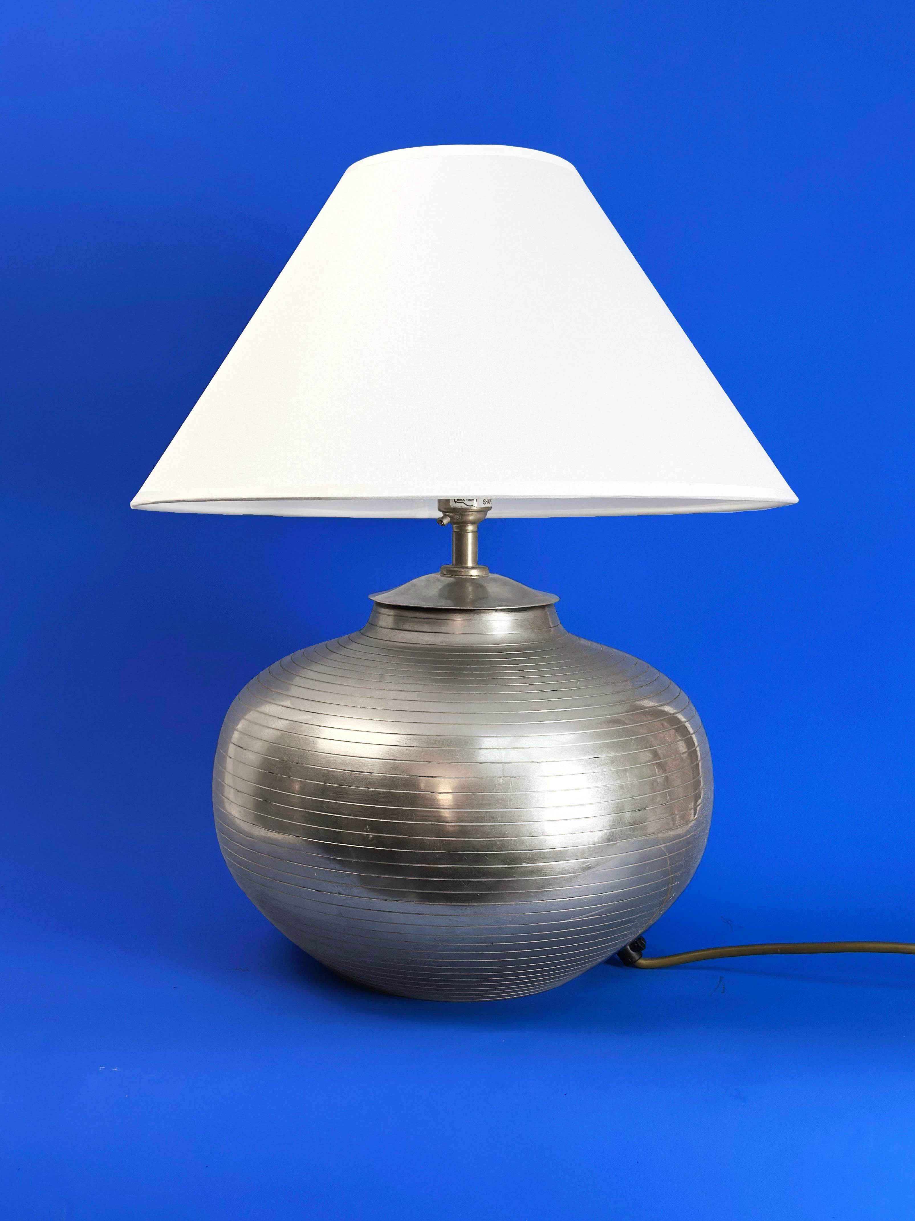 1980's hammered aluminium 'Modernist' style lamp

A hammered aluminium table lamp with a broad, urn-shaped base. Featuring deeply etched concentric lines rising from the base to the top of the lamp body, it offers a simple and textured look. Echoing