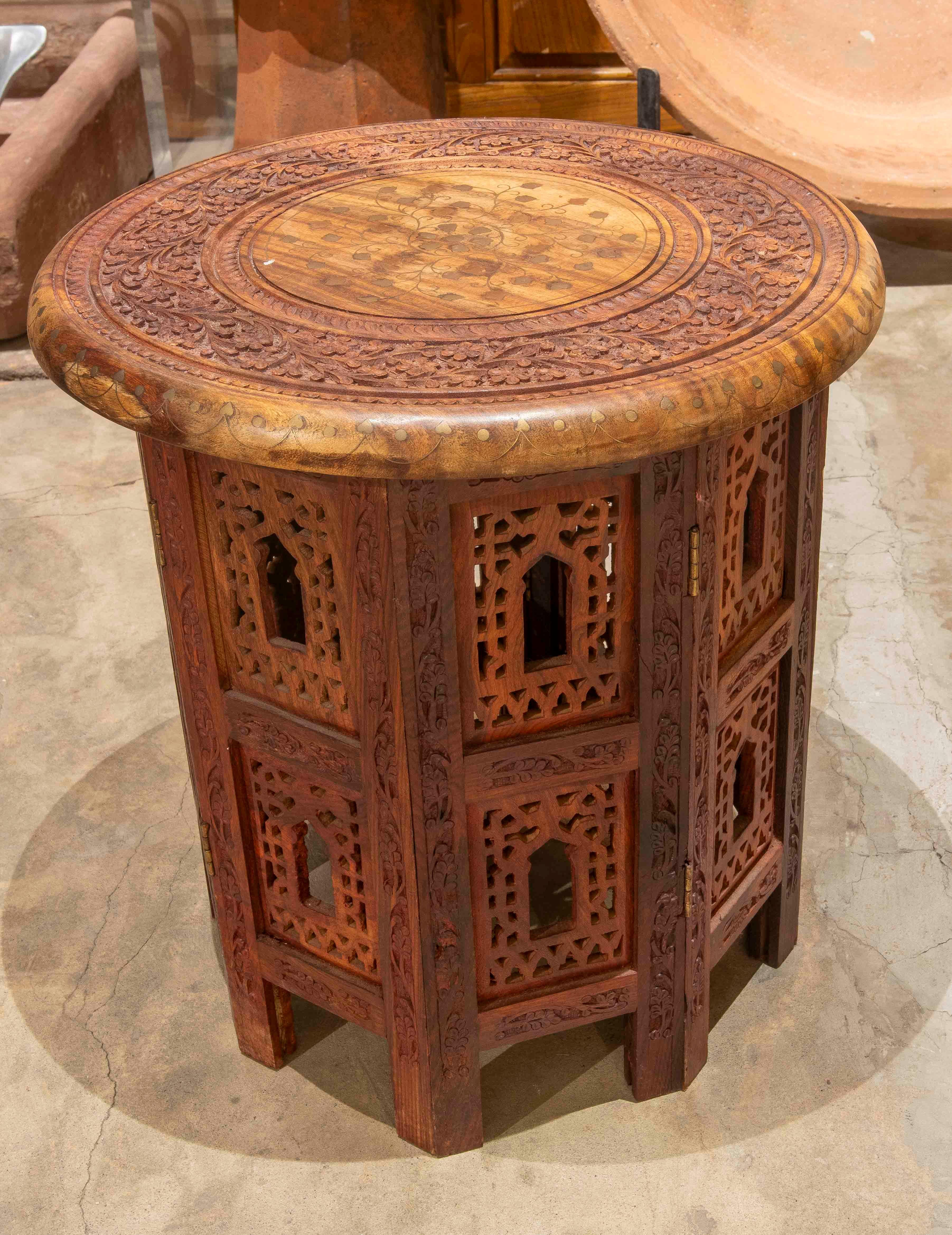 Stunning round side table crafted from hand-carved wood, featuring delicate marquetry and geometric and plant motifs clearly inspired by Moorish-Indian motifs.

The circular tabletop features an inlaid central design and a richly carved border with