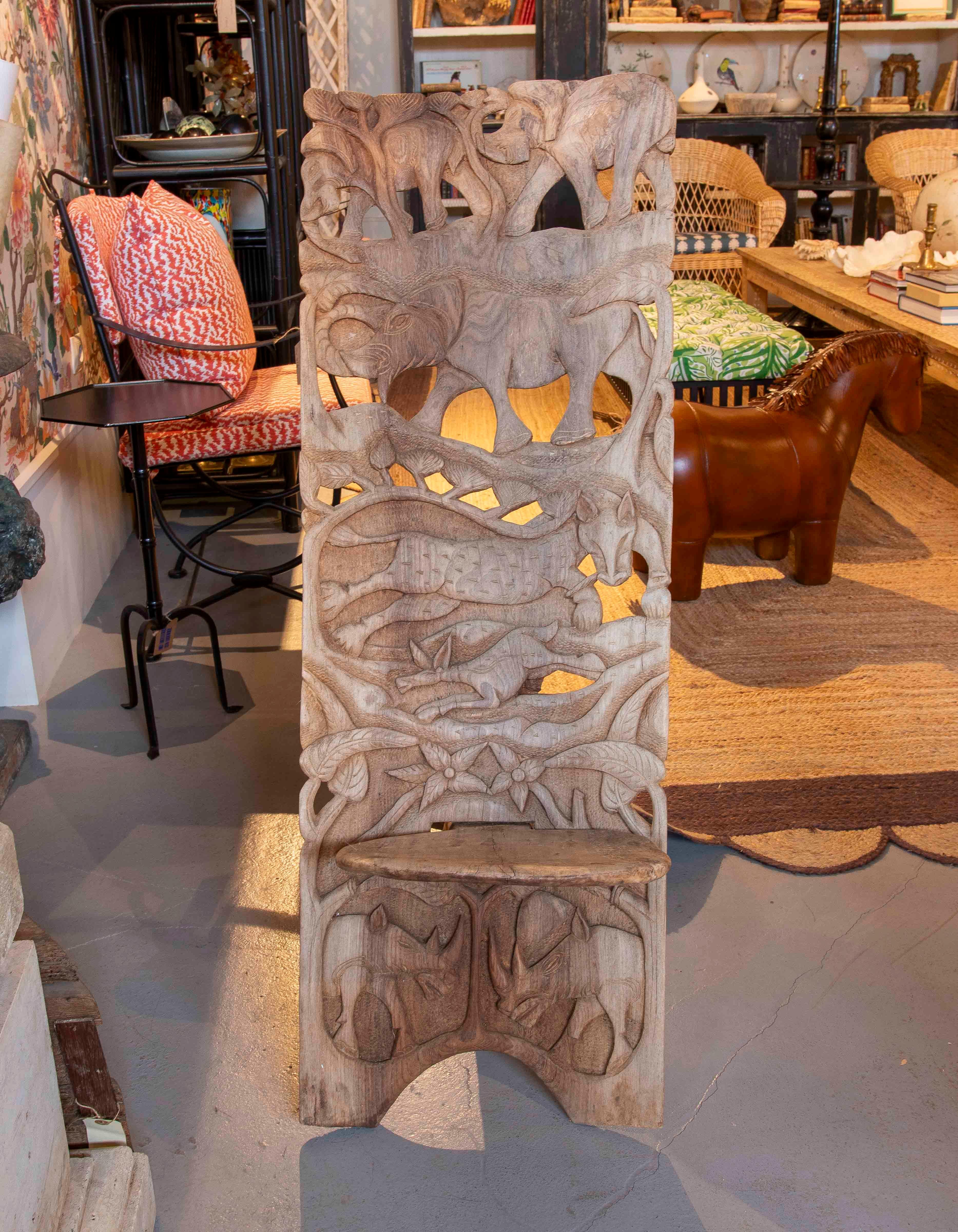 Spectacular solid wood chair with an intricate hand-carved design, depicting a wildlife scene with elephants, rhinos and other exotic animals. Its high, curved backrest makes it a piece of great decorative presence and comfort. Ideal for spaces with