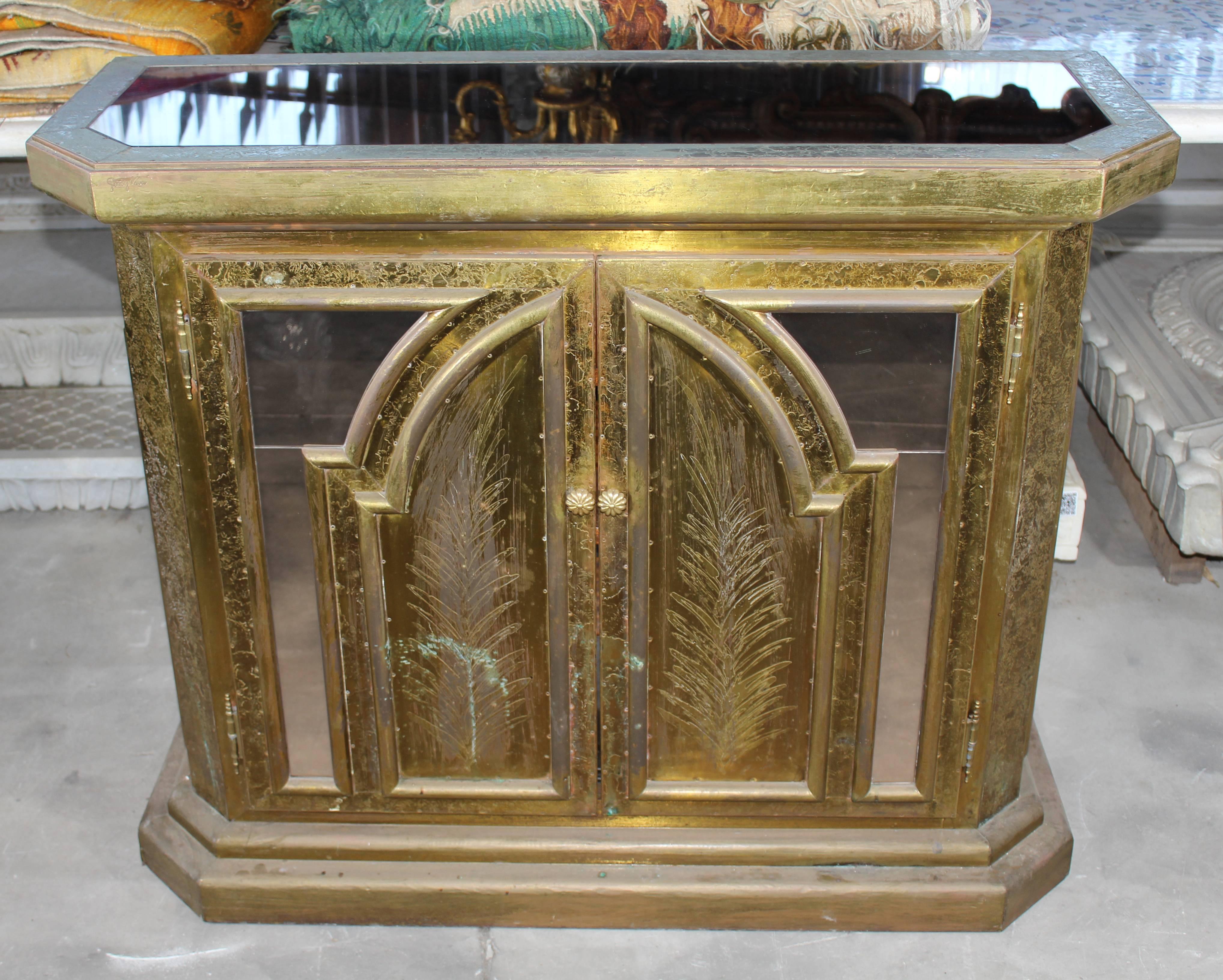 Two-door cabinet handcrafted in the 1980s shaping gilded brass over a wooden frame. Simple geometric style with oriental accents combining smoked glass in doors and top.