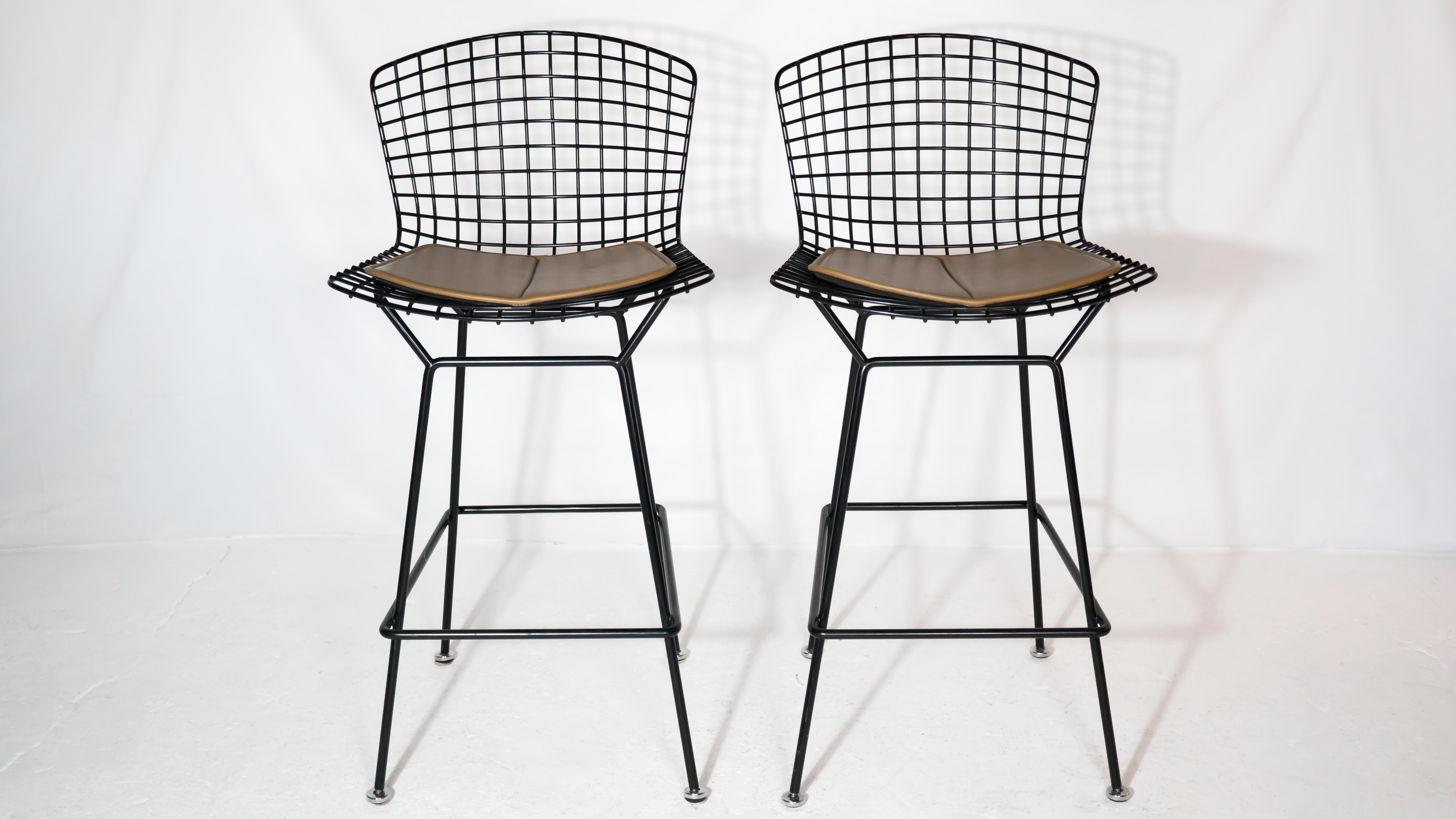 Pair of authentic Bertoia bar stools by Harry Bertoia for Knoll International, circa 1988. Black powder coated frame with original tan colored seat pad that snaps securely to the frame. In absolute pristine condition with no almost no signs of wear.