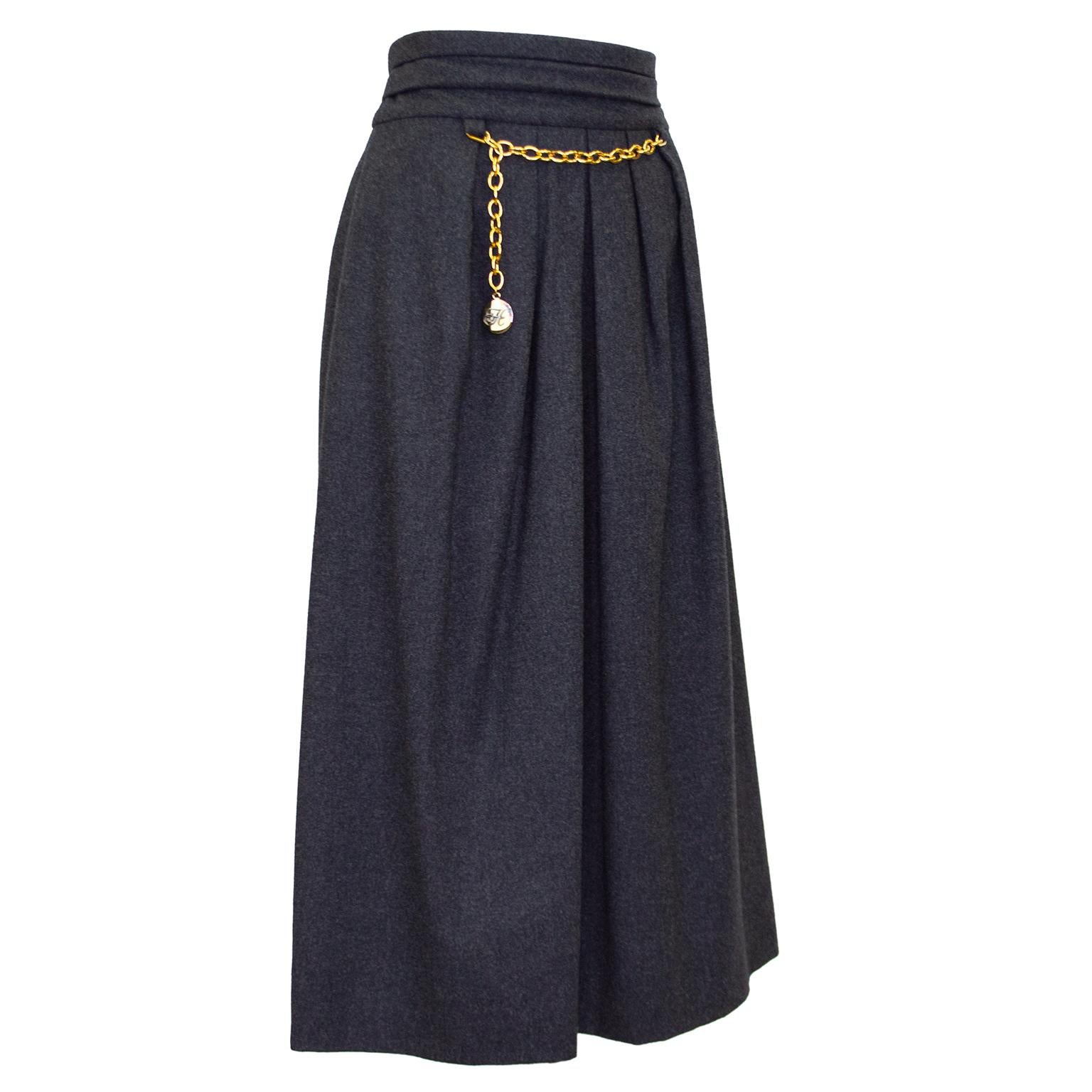 Beautiful Hermes dark grey skirt from the 1980s. High waisted with fold details, A-line shape with inverted pleats and midi length. 90% wool, 10% cashmere. Gold tone chain detail across front waist with round Hermes H hanging charm. Side zipper with