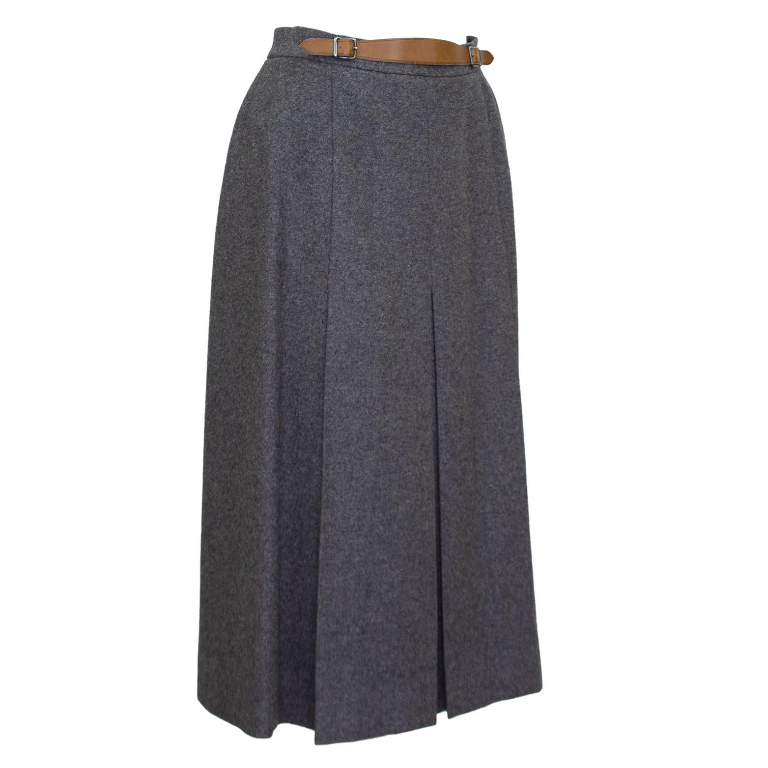 1980s Hermes grey wool skirt. High waisted with slight a-line shape with centre inverted box pleat. Tan leather detail at waist with tonal top stitching and silver metal buckles. Midi length. Side zipper with hook and eye. Excellent vintage