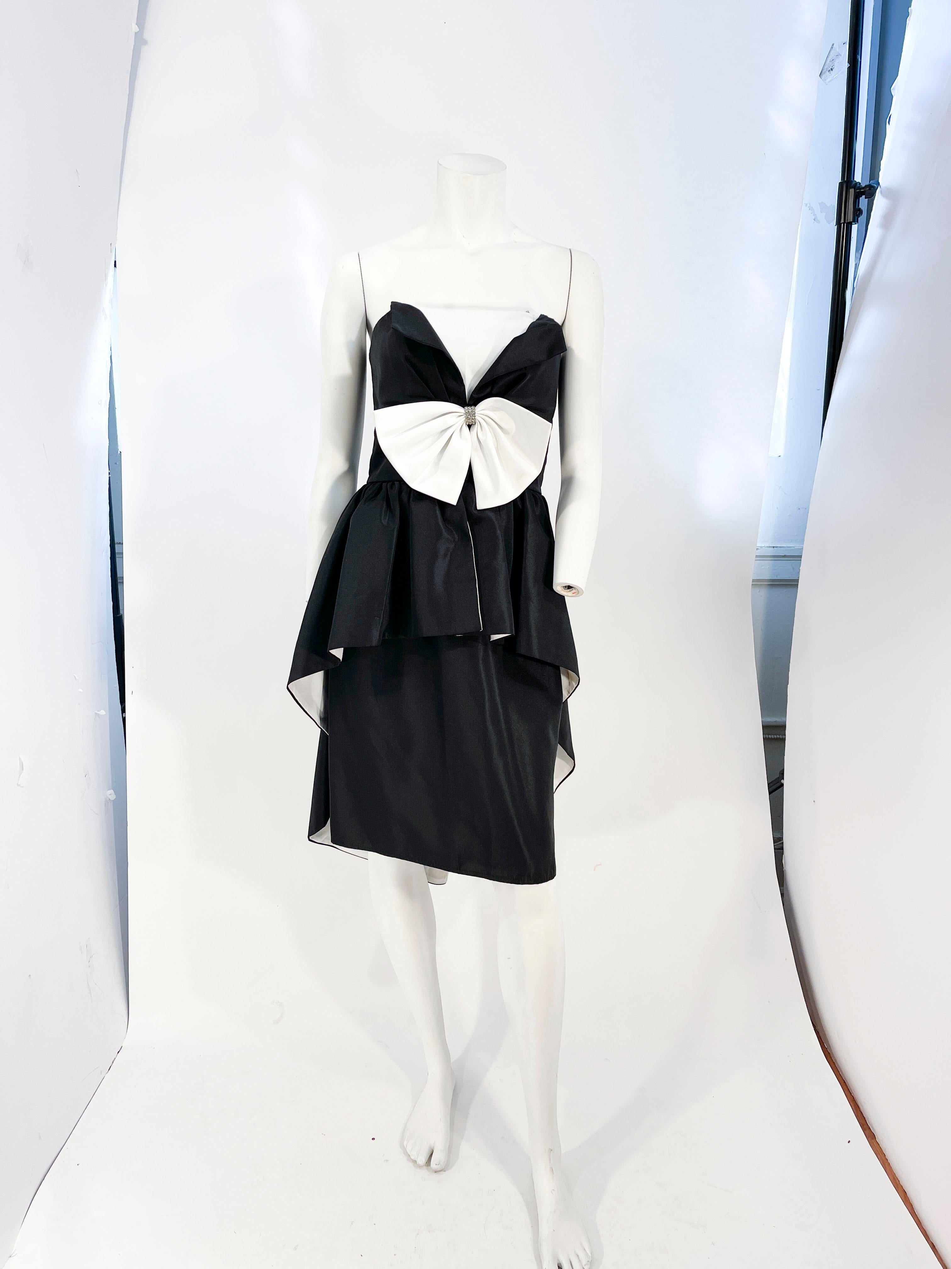 1980s Huey Waltzer for Darcy black and white cocktail dress featuring a fitted and layered bodice with black panels layered over the white bust line. Along the double bust line is an enlarged centered bow finished with a band of rhinestones. 

The