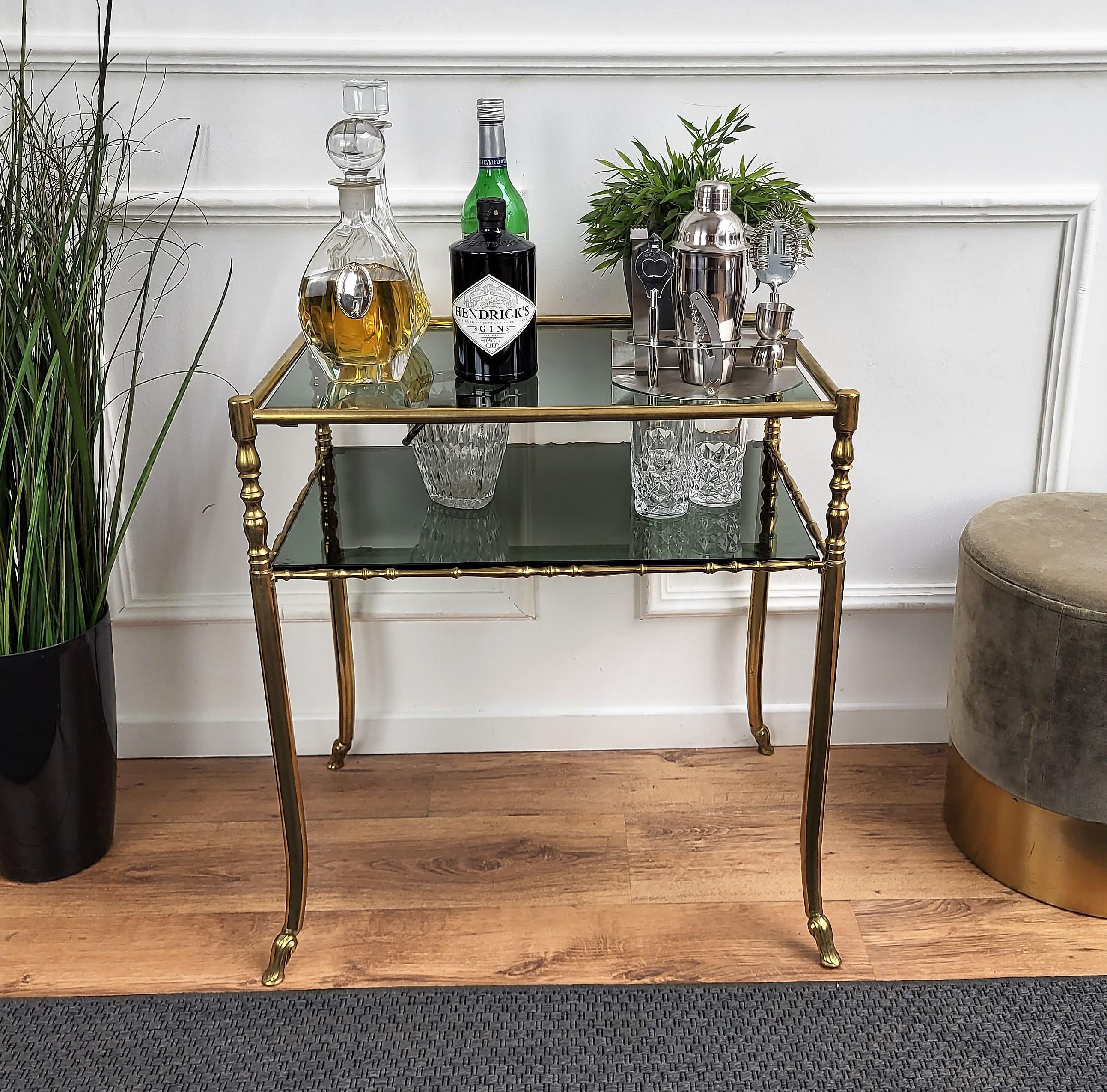 Beautiful and stylish vintage 1980s Italian brass side table or end table console with two smoked glass shelves ideal as well for dry bar cabinet. A great piece that perfectly adds to every home decor the typical glitz, glamour and gold of Hollywood