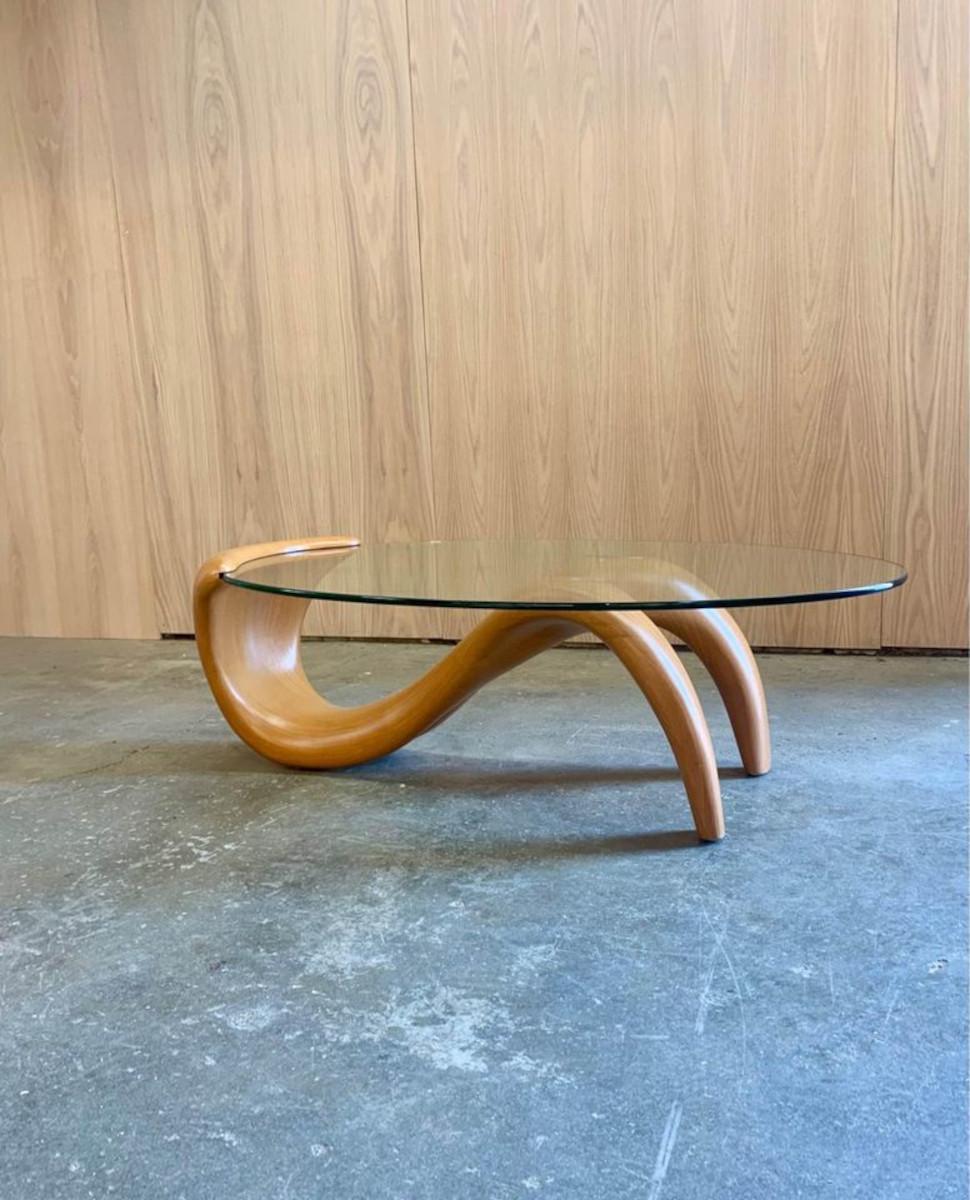 Have you ever seen such a thing? This incredibly unique coffee table, dating to the 1980s, features a free-flowing fiberglass base with a faux wood finish. The thick plate glass surface nestles seamlessly within the base, creating an intriguing