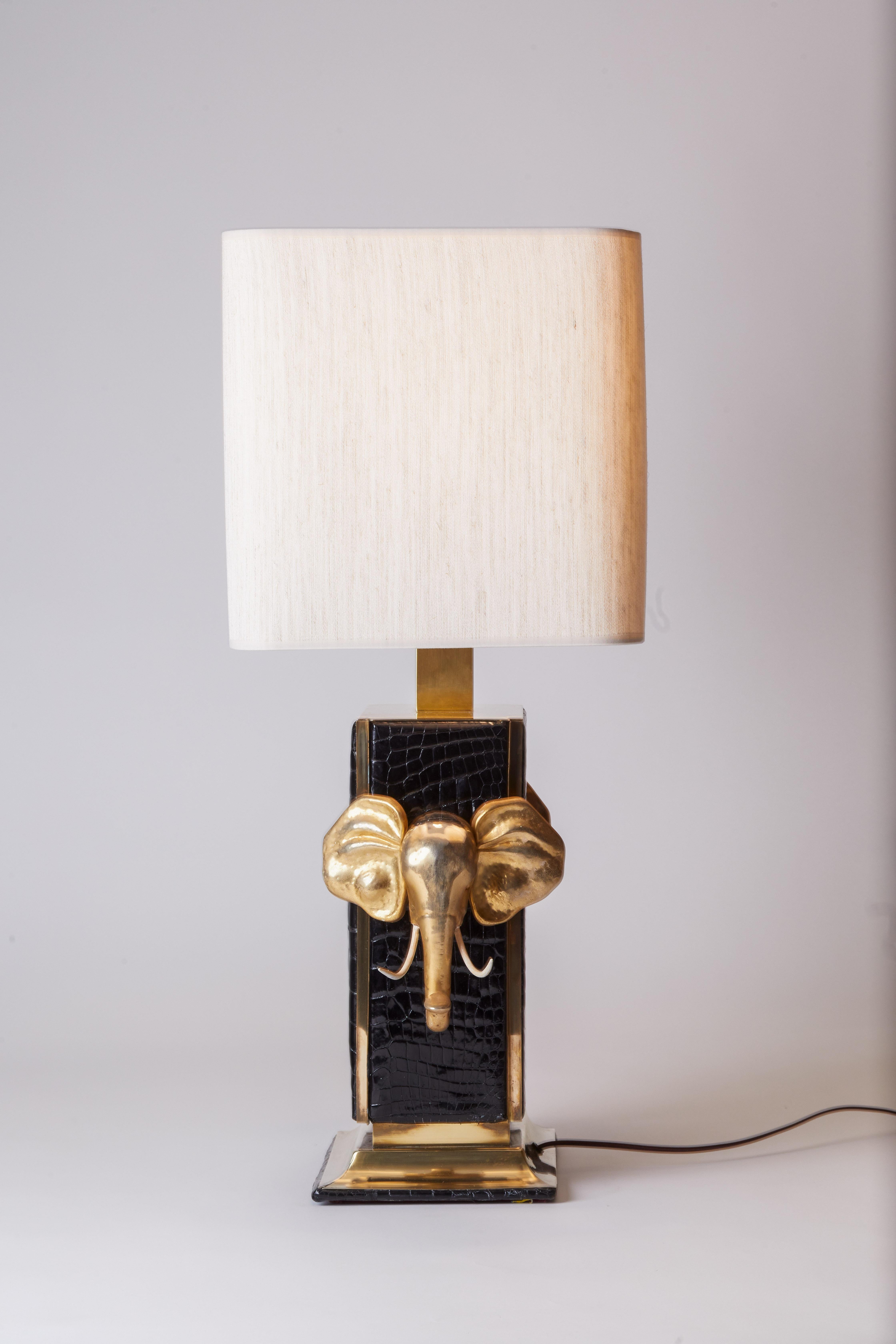Unique 1980s Italian black crocodile covered brass lamp with elephant head detailing on either side. Brass base and custom lampshade. Excellent condition.