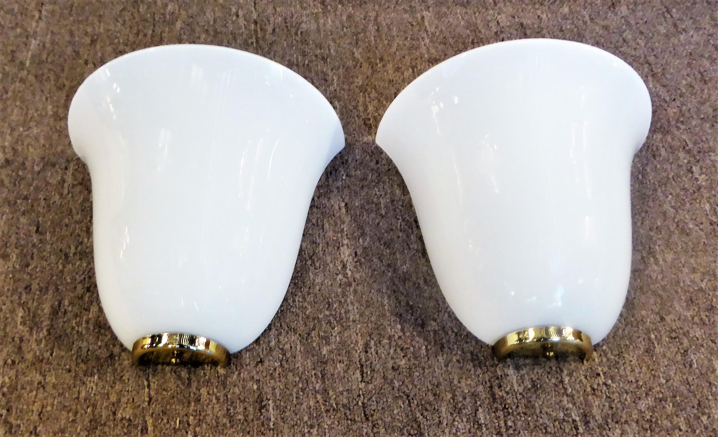Beautiful and Classic, this pair of blown glass sconces feature a white cased glass bell shaped globe. An up light as well, they have a half bowl shape flared at the top with a brass socle bottom. Each fixture takes a plug in fluorescent bulb and is