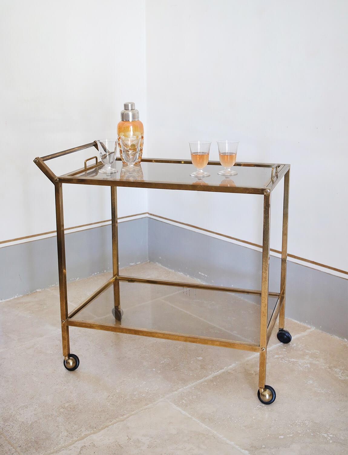 Gorgeous 1980s Italian drinks trolley / bar cart in brass and glass. The trolley has two glass shelves, a strong brass frame and beautiful brass bolts detail. The top glass shelf cleverly lifts off to make a glass tray with two handles. This piece