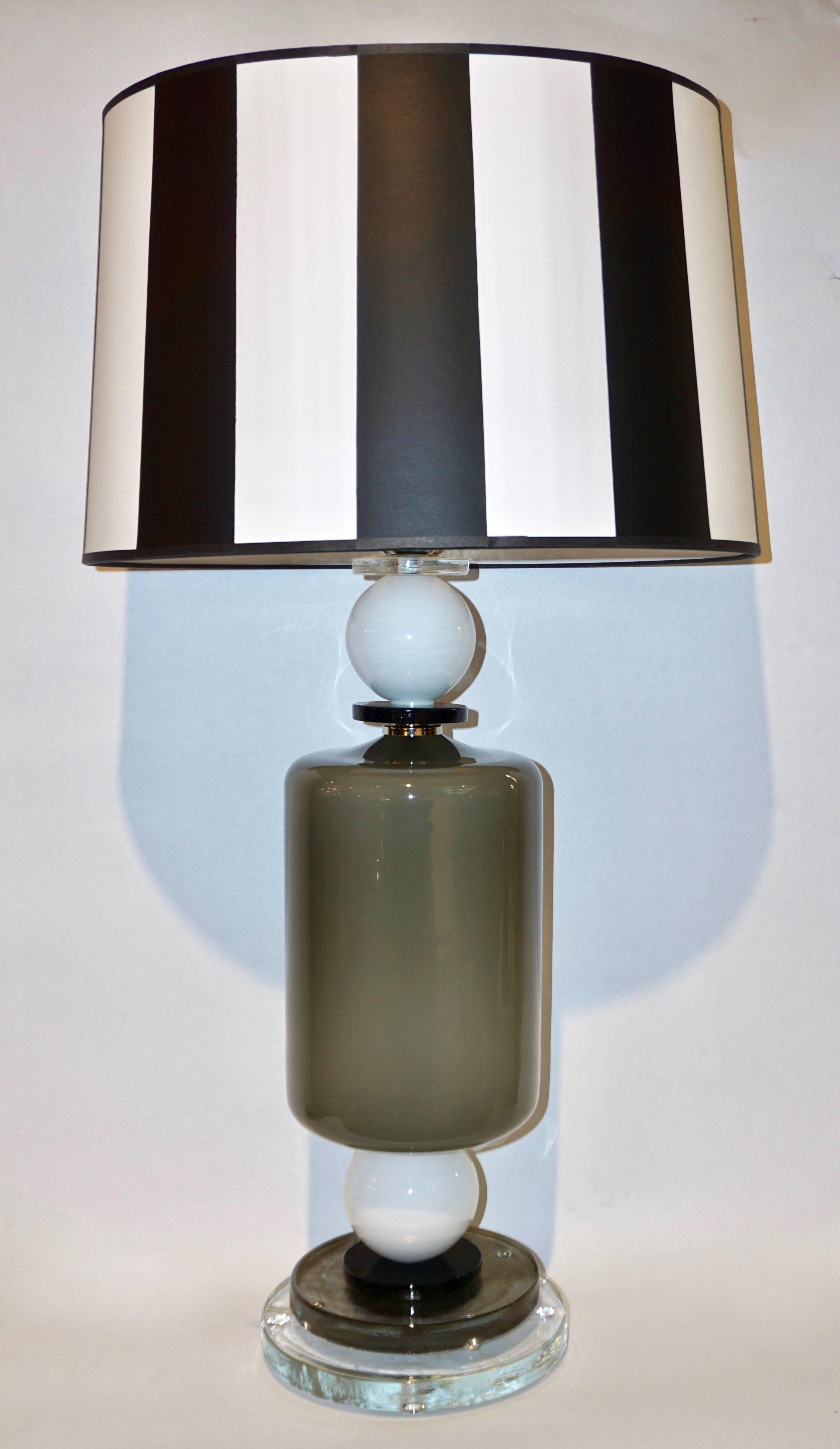 A fine Italian Design pair of modern table lamps of geometric shapes. The central cylindrical body in radiant grey blown Murano glass highlighted with two white spheres and black round accents is supported by a high quality stepped round base,