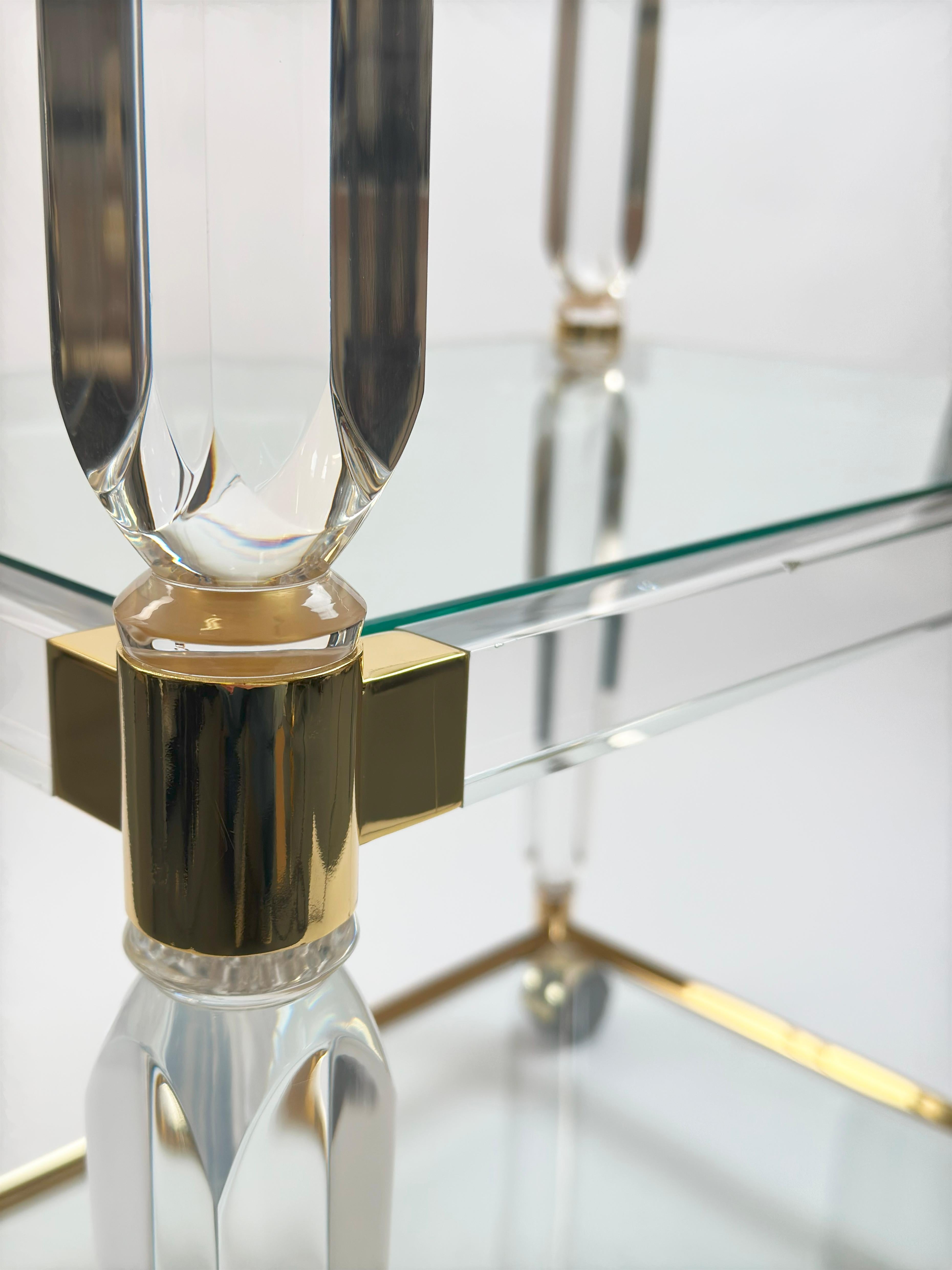 Llamativo carrito de bar italiano vintage de los años 80, esta pieza capta la esencia del estilo Hollywood Regency con su perfil escultural y su juego de materiales luminosos.

La montura está fabricada en Lucite cristalino, acentuado con herrajes