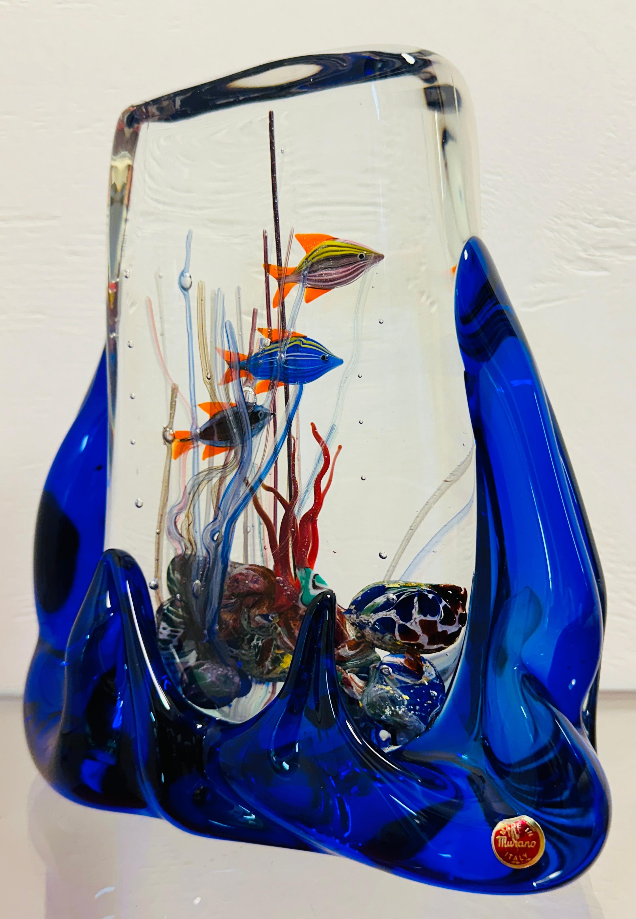 Un acquario in vetro di Murano soffiato a mano incredibilmente dettagliato con tre pesci a strisce con code e pinne arancioni.  Le conchiglie e i coralli multicolore si trovano sul fondo dell'acquario e brillano grazie alle inclusioni in argento e