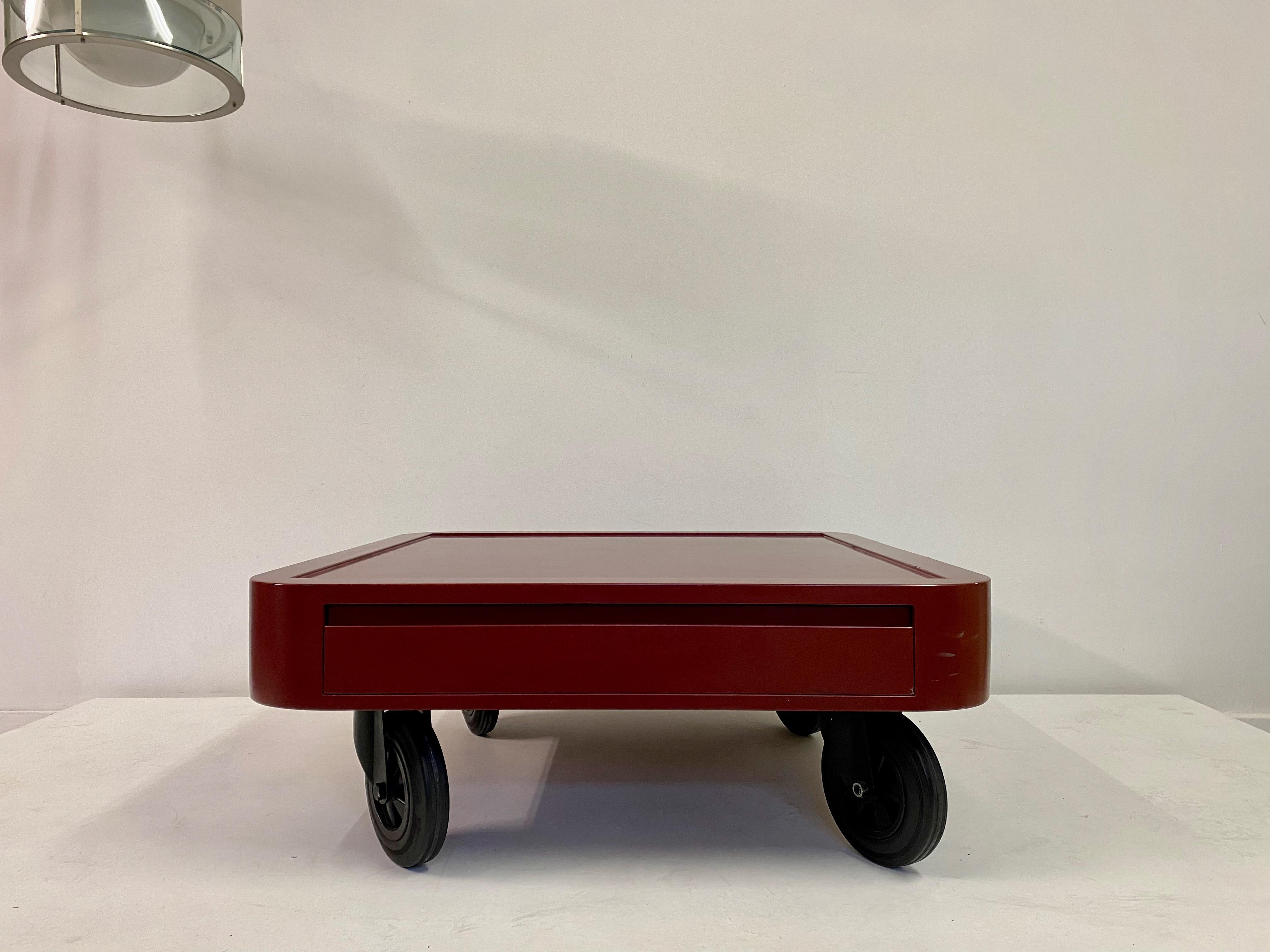 Table basse

Sur des roues en caoutchouc

Stratifié rouge

Un tiroir

L'Italie des années 1980