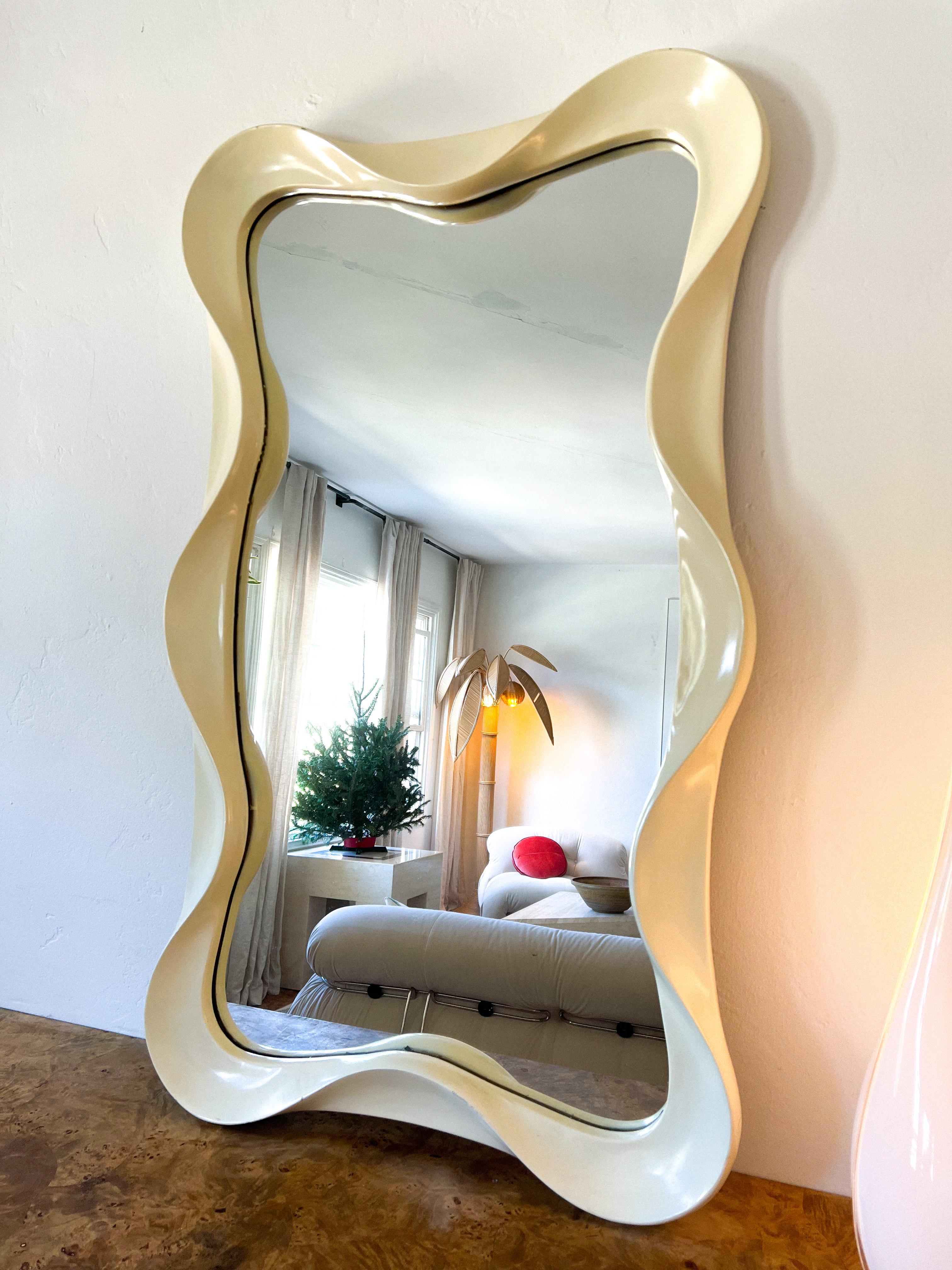 This vintage Italian wall mirror features a wavy, fluid frame crafted from lacquered wood in a warm, creamy tone. Its bold silhouette and playful curves evoke the iconic postmodern aesthetic of Ettore Sottsass and the Memphis Milano design