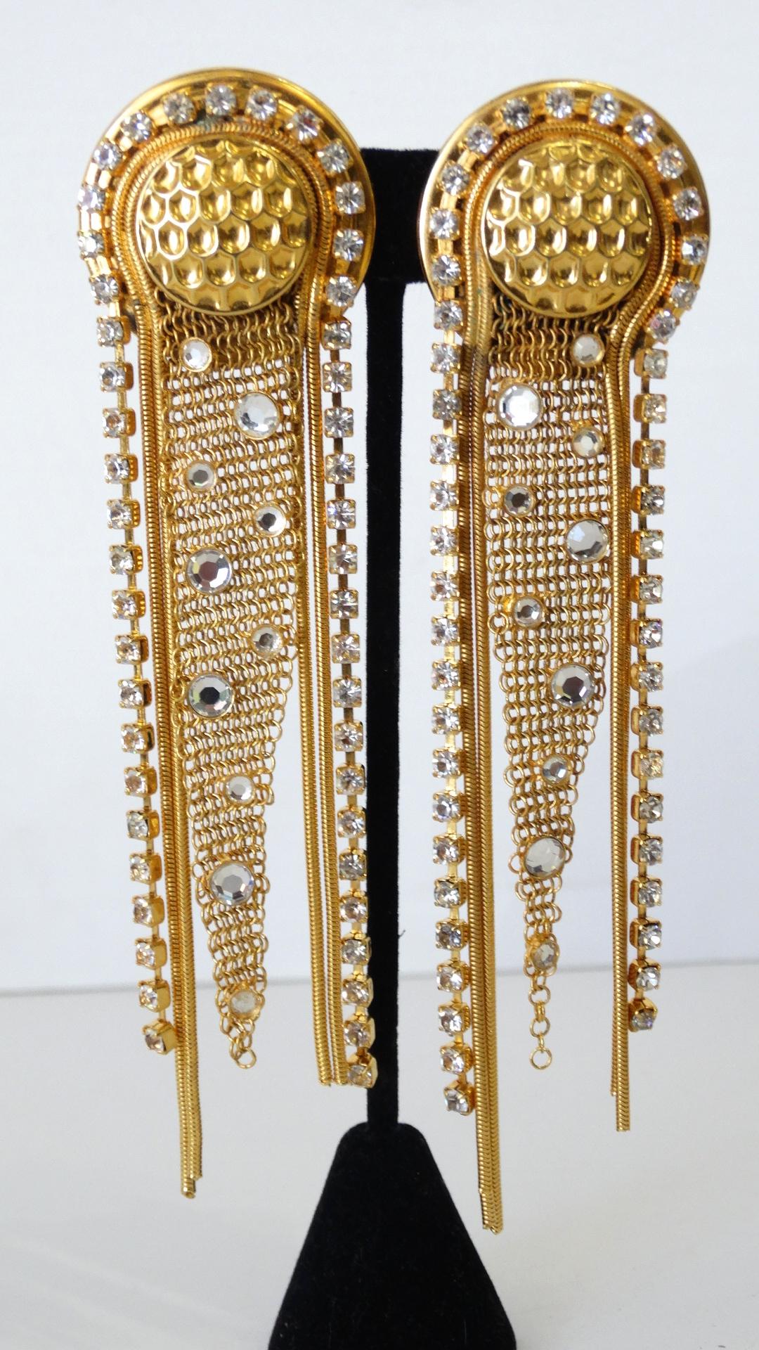 The Perfect Pair Of Earrings For All Of Your Outfits! Circa 1980s, these Jack Smile clip-on earrings features a scale textured circular setting with rhinestone and gold plated strands draping over the top and hanging down. A piece of asymmetrical