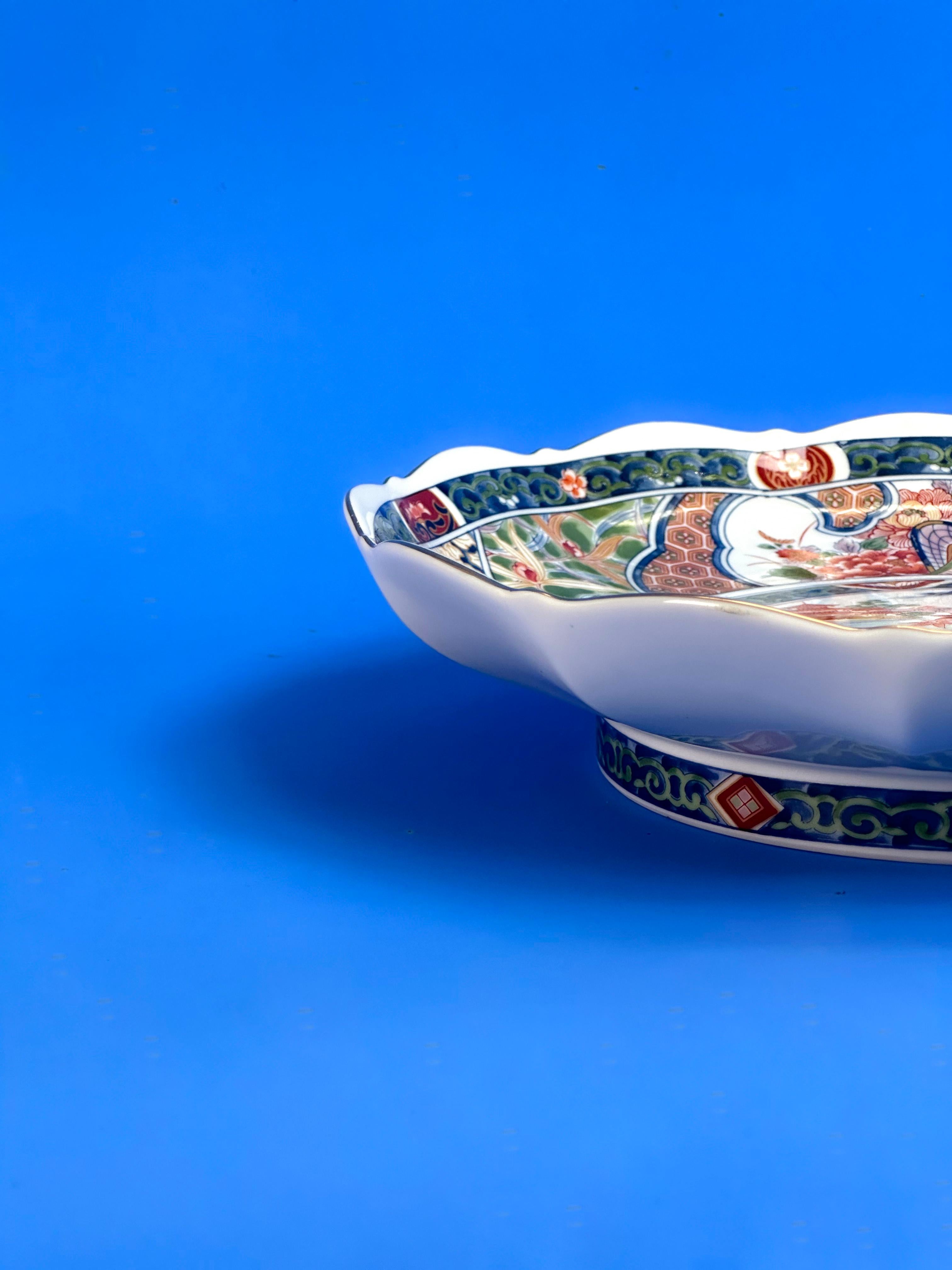 Eine japanische Porzellan-Servierplatte im Vintage-Stil.

Die in den 1980er Jahren in Japan handgefertigte Servierplatte zeigt eine aufwendige japanische Szene und Ornamente, die auf einem traditionellen Imari-Muster basieren und in traditionellen