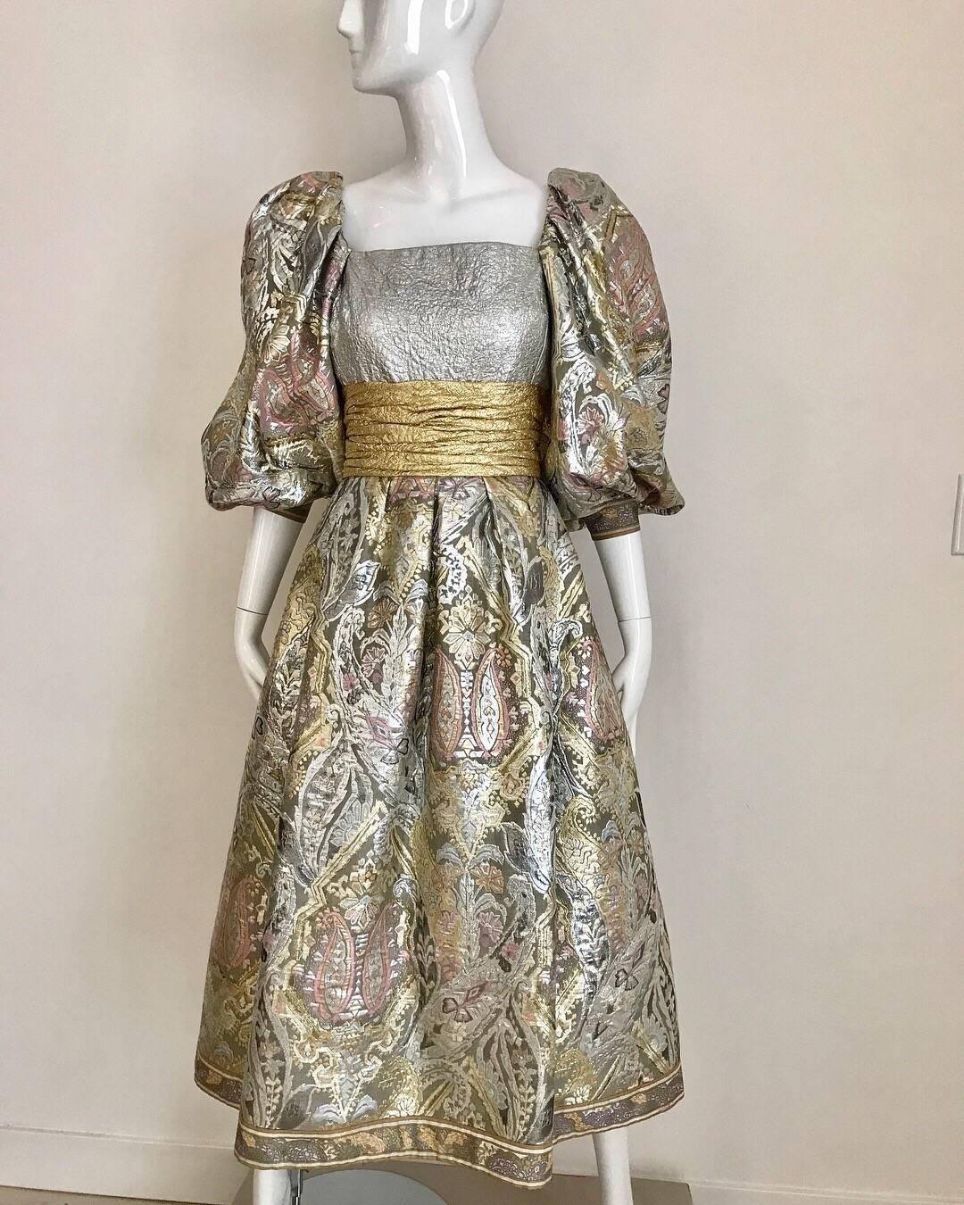 Dramatic vintage Leonard Brocade floral in dress in pink, silver grey metallic and large gold cummerbund  belt style. Sleeves can be worn off shoulder. Lined in silk.
Size: Medium 
Bust: 34” fit C cup/ or 36”
Waist: 30” / Dress length: 43”/ Sleeve