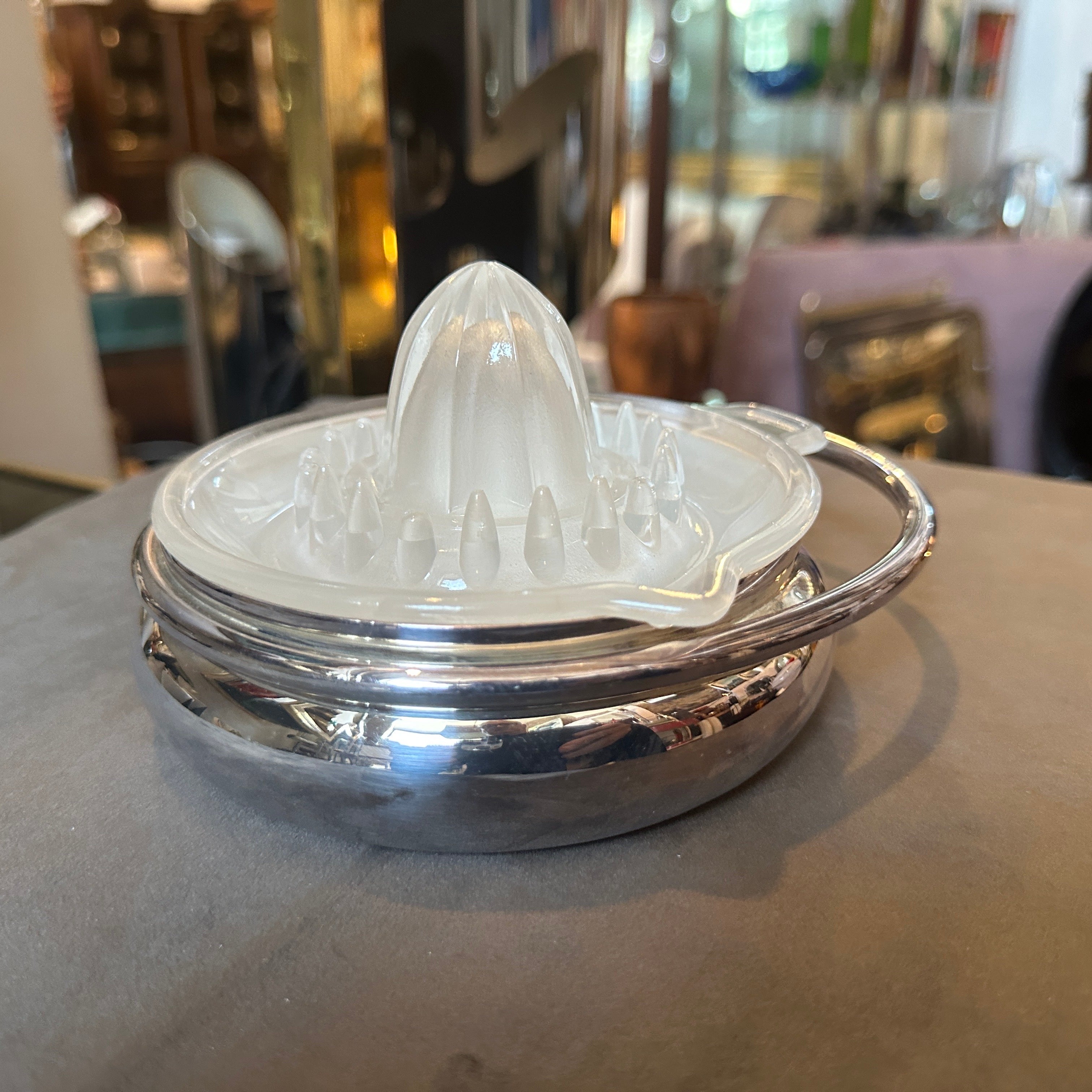 This is a 1980s modernist citrus squeezer designed by Lino Sabattini, a renowned Italian designer known for his work in metalware. The piece is characterized by its sleek, functional design typical of modernist aesthetics. The citrus squeezer has a