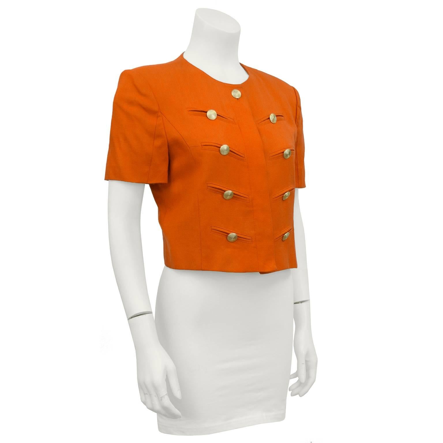 Orange short sleeved Louis Feraud military style cropped jacket from the 1980s. Gold coiled rope buttons over faux slit pockets accent the front. Buttons hidden under the front placket close the jacket. In excellent condition. Extra button included