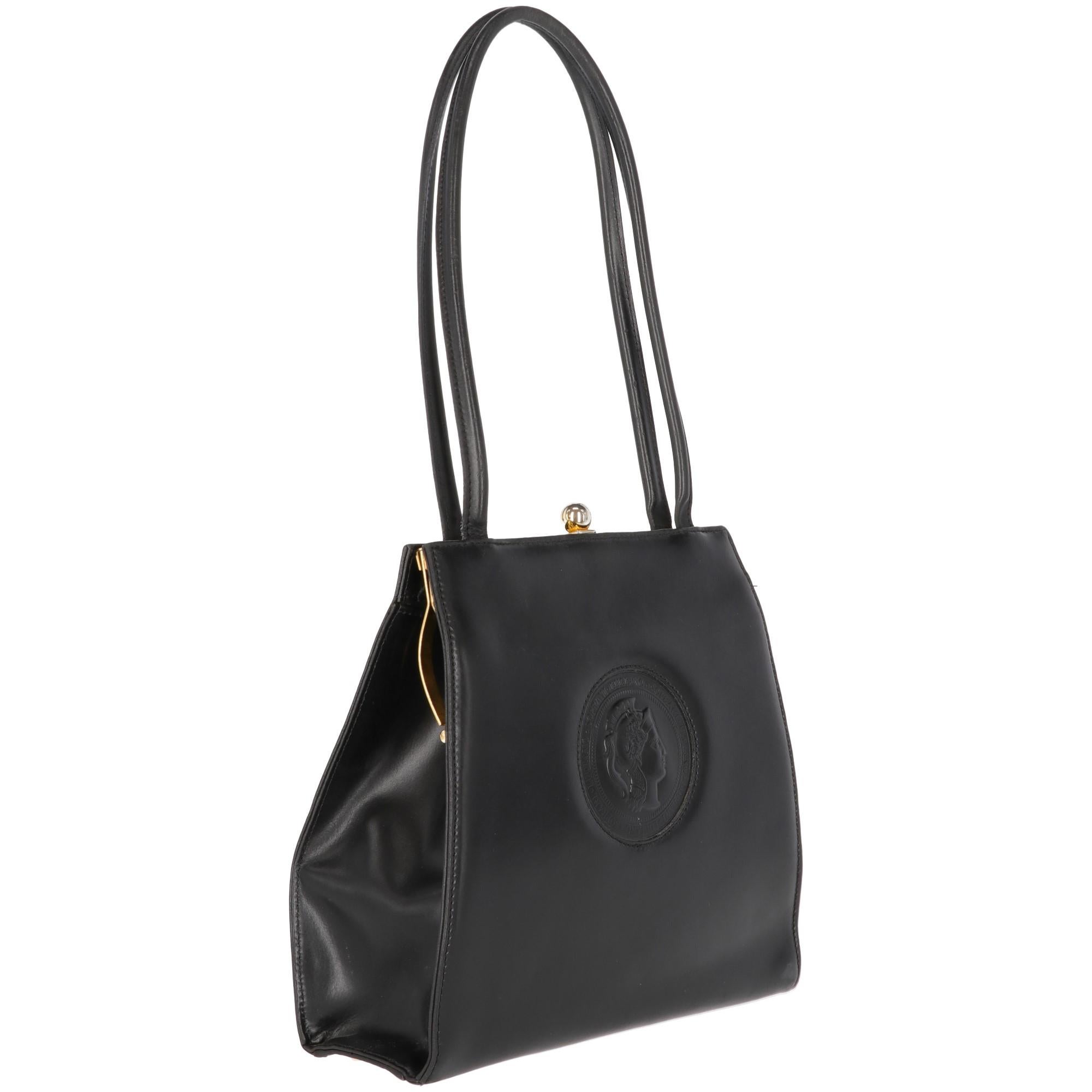 The Luciano Soprani black leather handbag features classic handles and an elegant gold-tone clasp closure.  The bag is embellished by an embossed logo on the front.  With branded jacquard lining and inner zip-pocket, this item is from 1980s