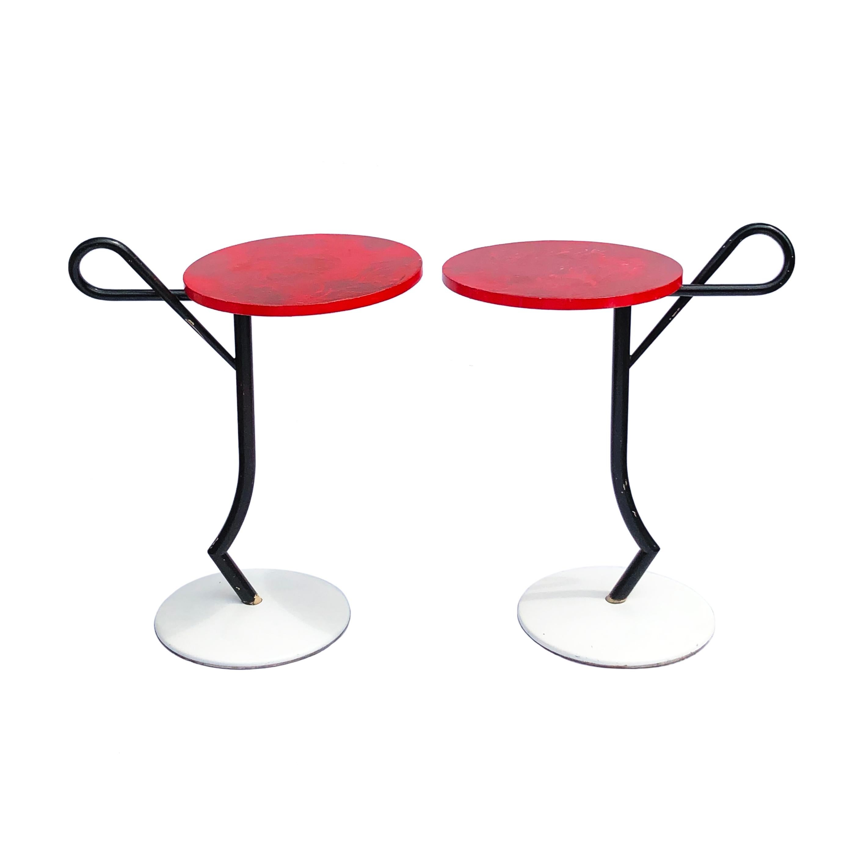 A unique pair of modernist side tables made in the 1980s and in the style of Memphis Design. Black curved rod iron frame with a bended handle on top of a white round plastic base with iron weights below supporting the red round table tops. The table