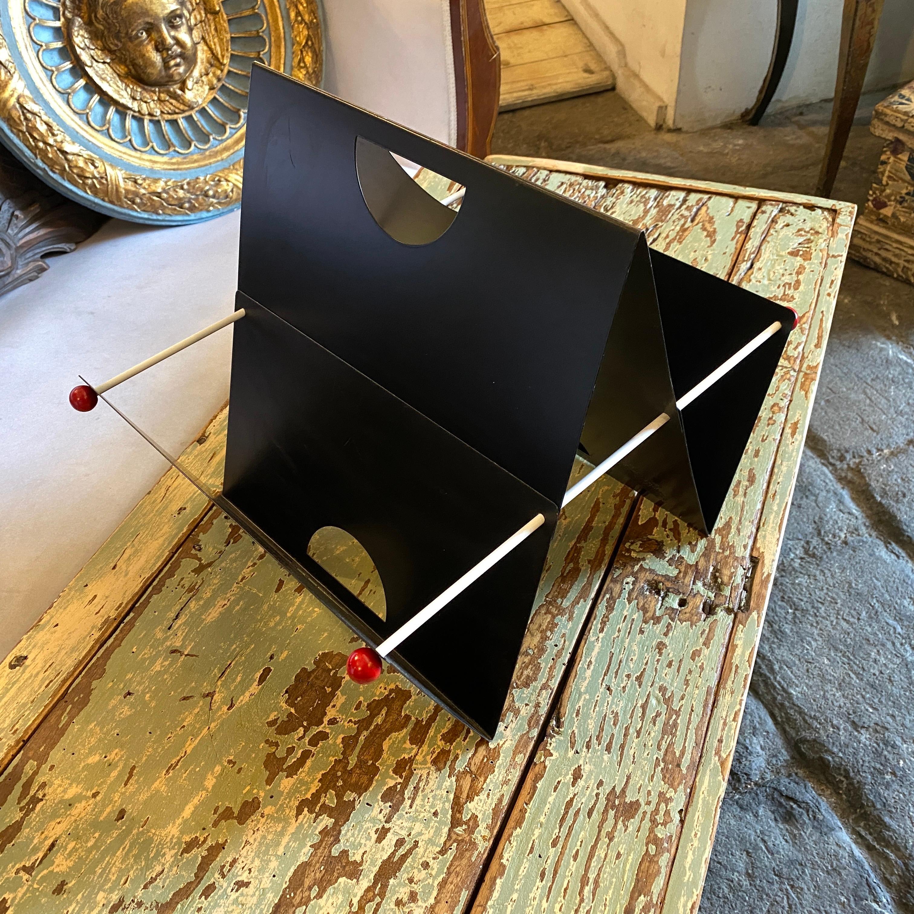 A painted metal magazine rack made in Italy in the style of Memphis Milano, signs of use and age. The three V-shaped pieces are pierced through by two metal bars from each side.