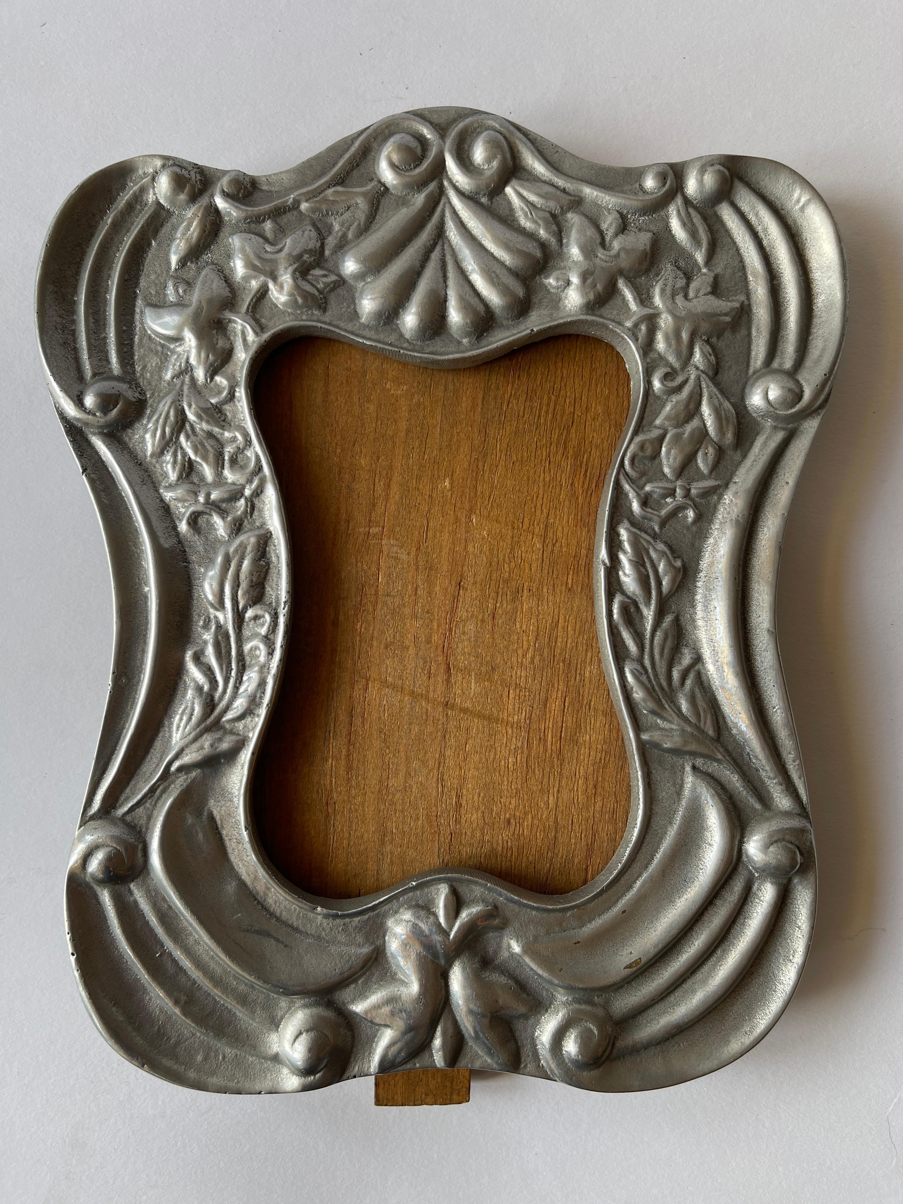  Marco de estaño curvado de diseño colonial español con trasera de madera. 
 El centro superior tiene un gracioso motivo de caracolas y motivos florales a los lados. 
Fabricado en México, c. 1980.
