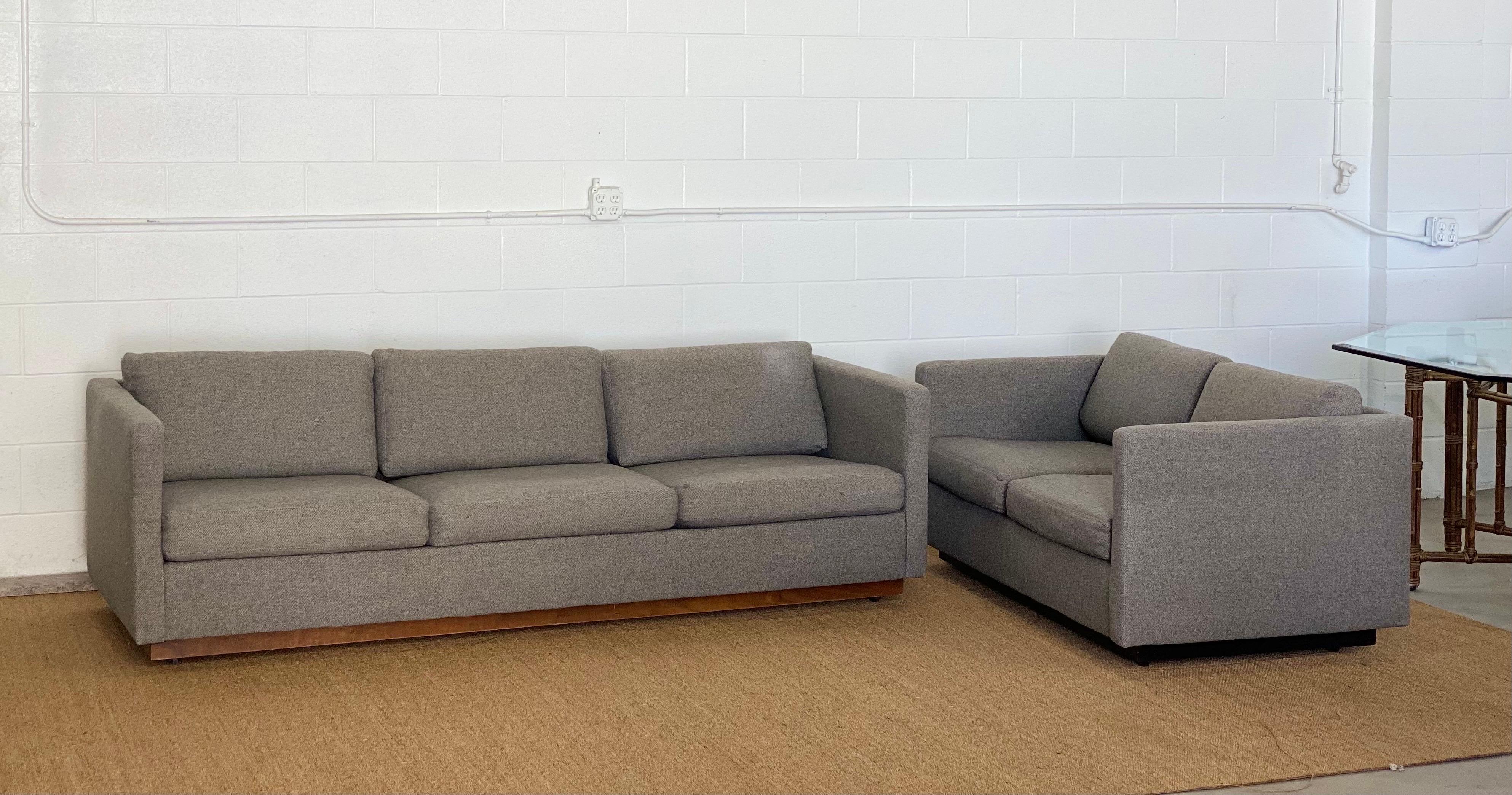 We are very pleased to offer a chic tuxedo sofa by American designer Milo Baughman for Thayer Coggin, circa the 1980s. This sofa showcases a wraparound frame and loose cushions upholstered in a grey fabric supported by a brown hardwood plinth base.