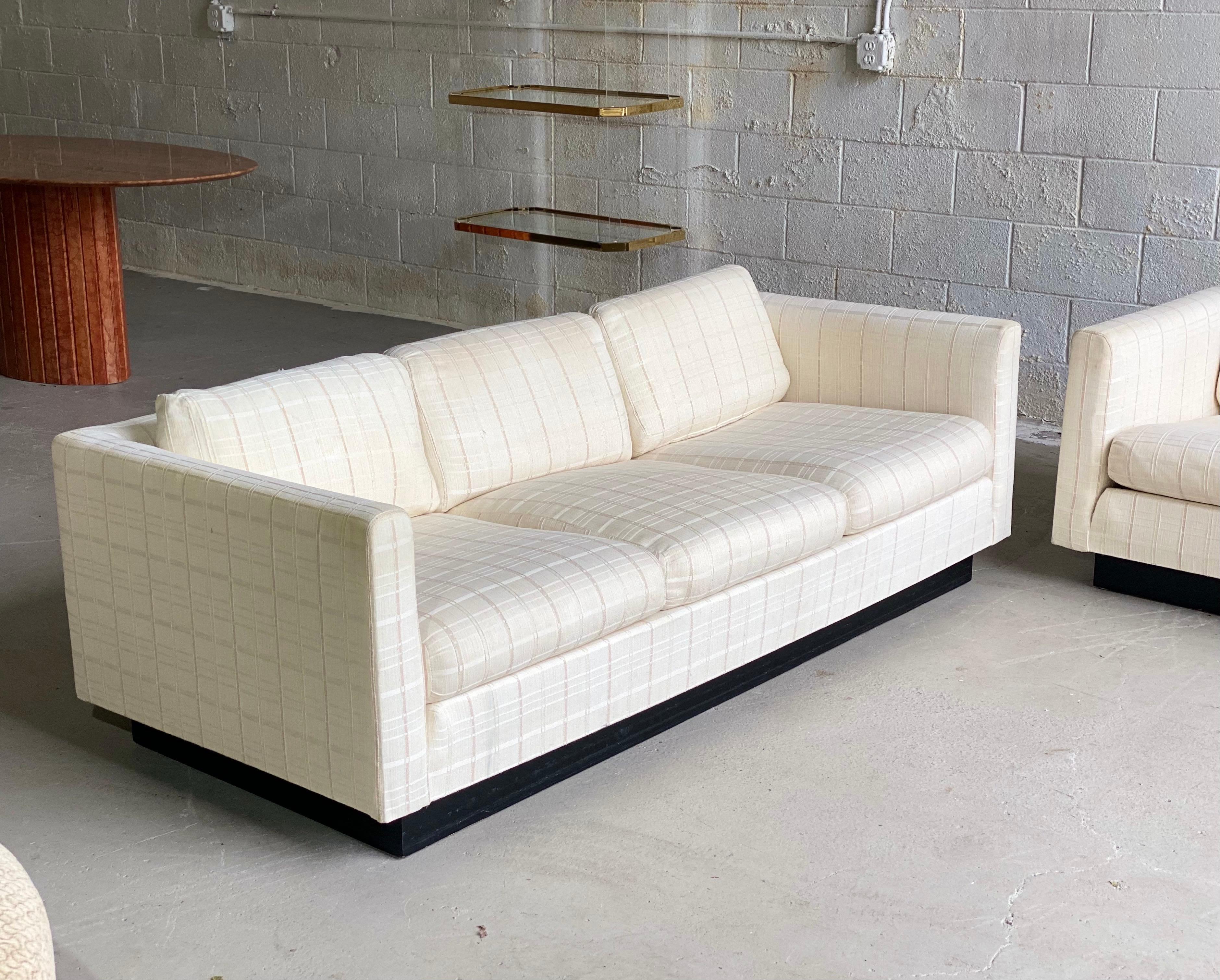We are very pleased to offer a pair of super chic, tuxedo sofas designed by Milo Baughman for Thayer Coggin, circa the 1980s. This set showcases a wraparound frame upholstered in a beautiful neutral linen fabric supported by a black plinth base.